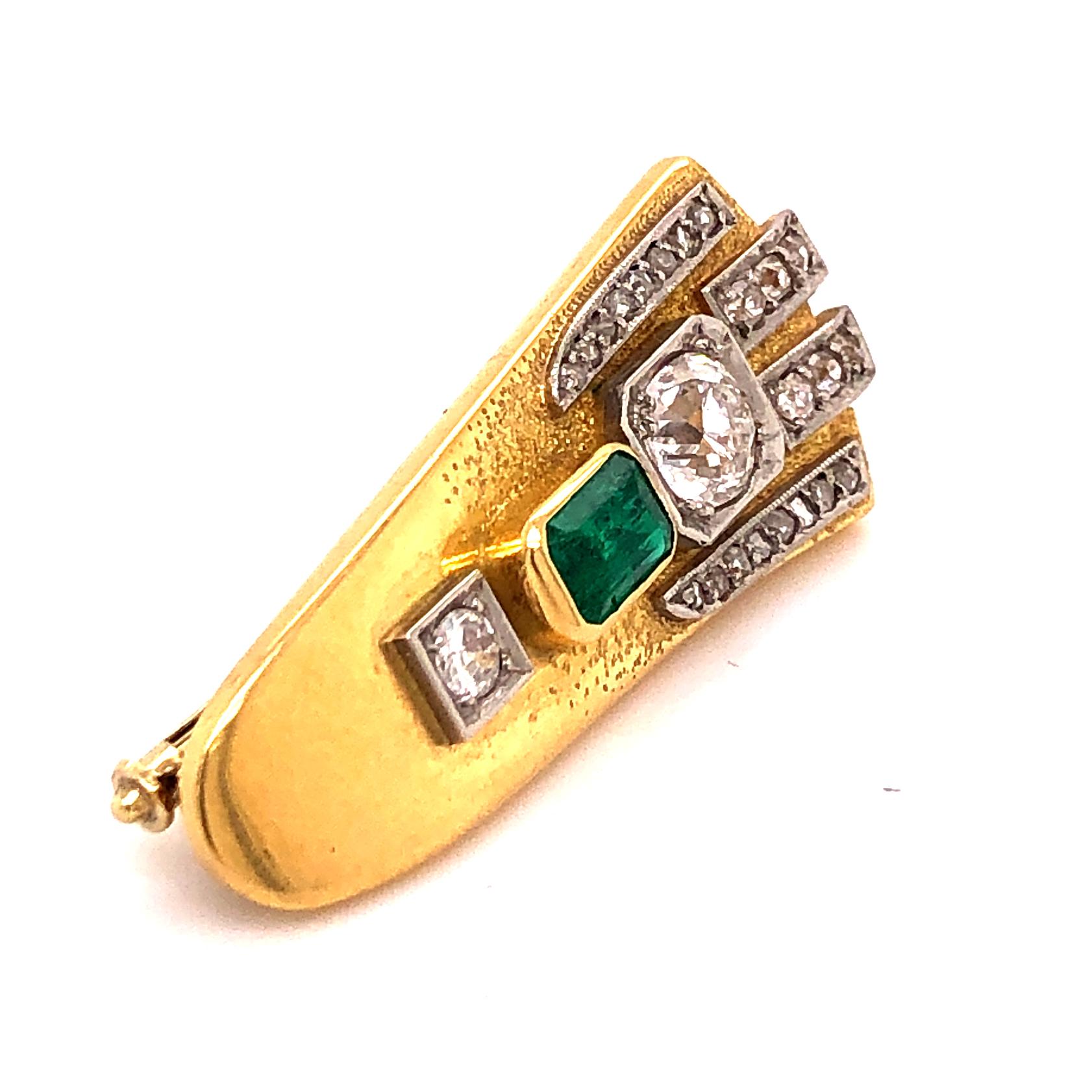 A lovely brooch in yellow gold with a Columbian emerald and old European cut diamonds. The big centre stone weighs approximately 0.6 carats. The brooch is in 18k yellow gold and it has an abraded gold design at the top. The clip mechanism is in 14k