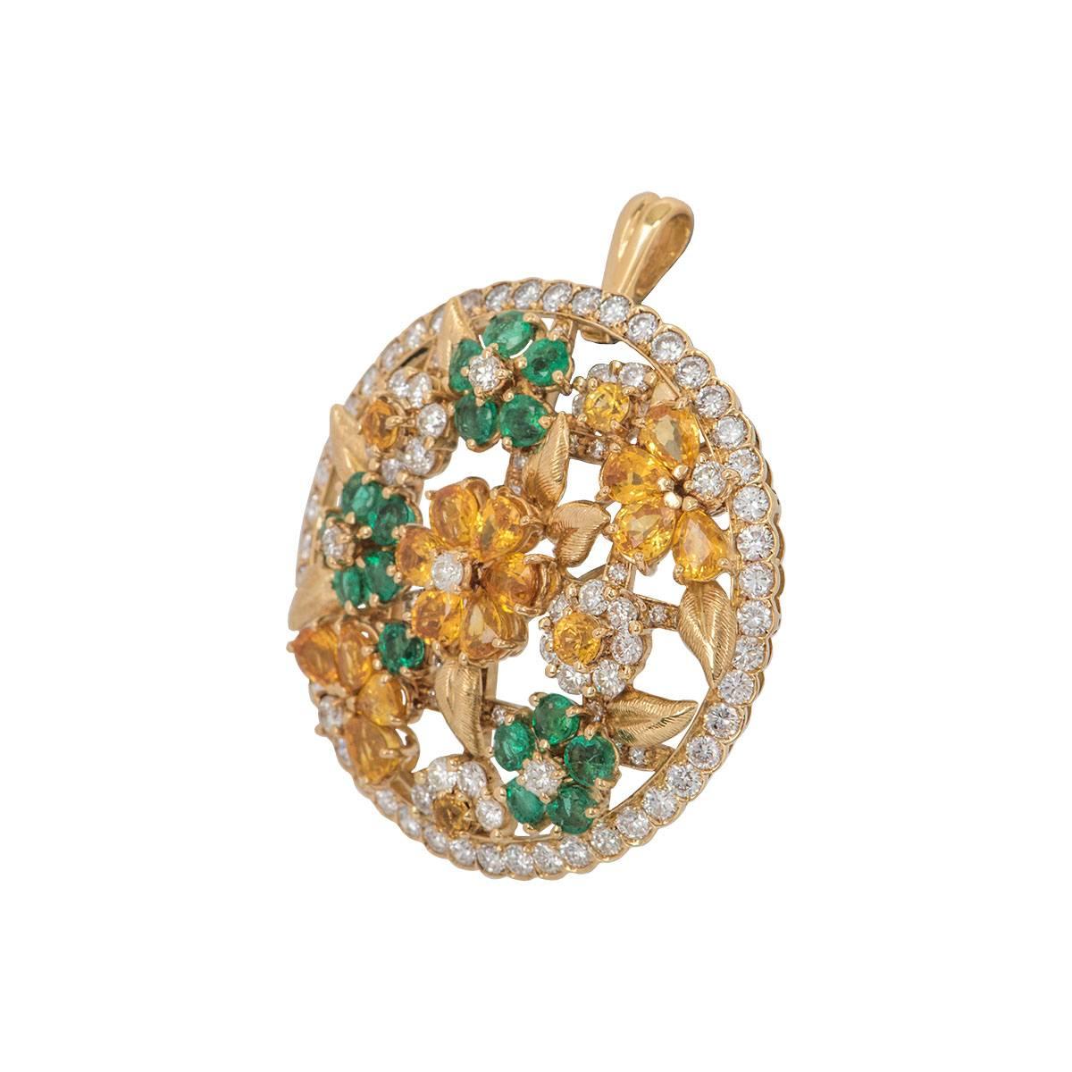 A large 18k yellow gold floral pendant/brooch. The pendant/brooch features an open work circular motif with round brilliant cut diamonds around the outer edge in a rub over setting. The centre of the pendant/brooch consists of a floral design set