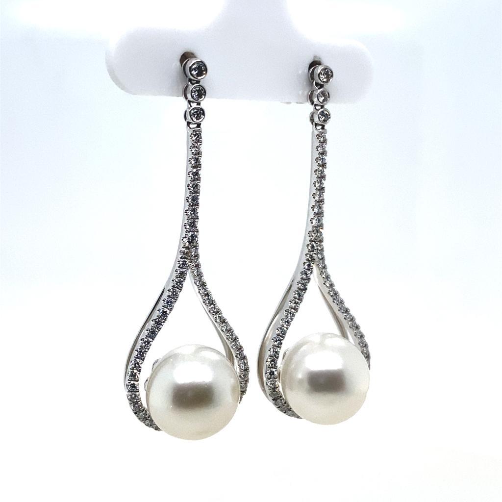 A pair of diamond and pearl drop earrings in 18 karat white gold.

Each classic and contemporary earring is designed with a round cultured pearl set in an illusion white gold basket setting within an an elegant pear shaped diamond frame claw set