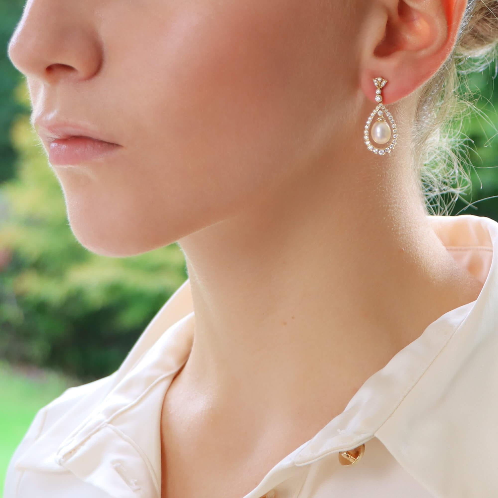A beautiful pair of diamond and pearl garland drop earrings set in 18k yellow gold.

Each earring prominently features a 6 x 8-millimetre pearl that elegantly hangs within a circular diamond set garland motif. To the top of the pearl is a single