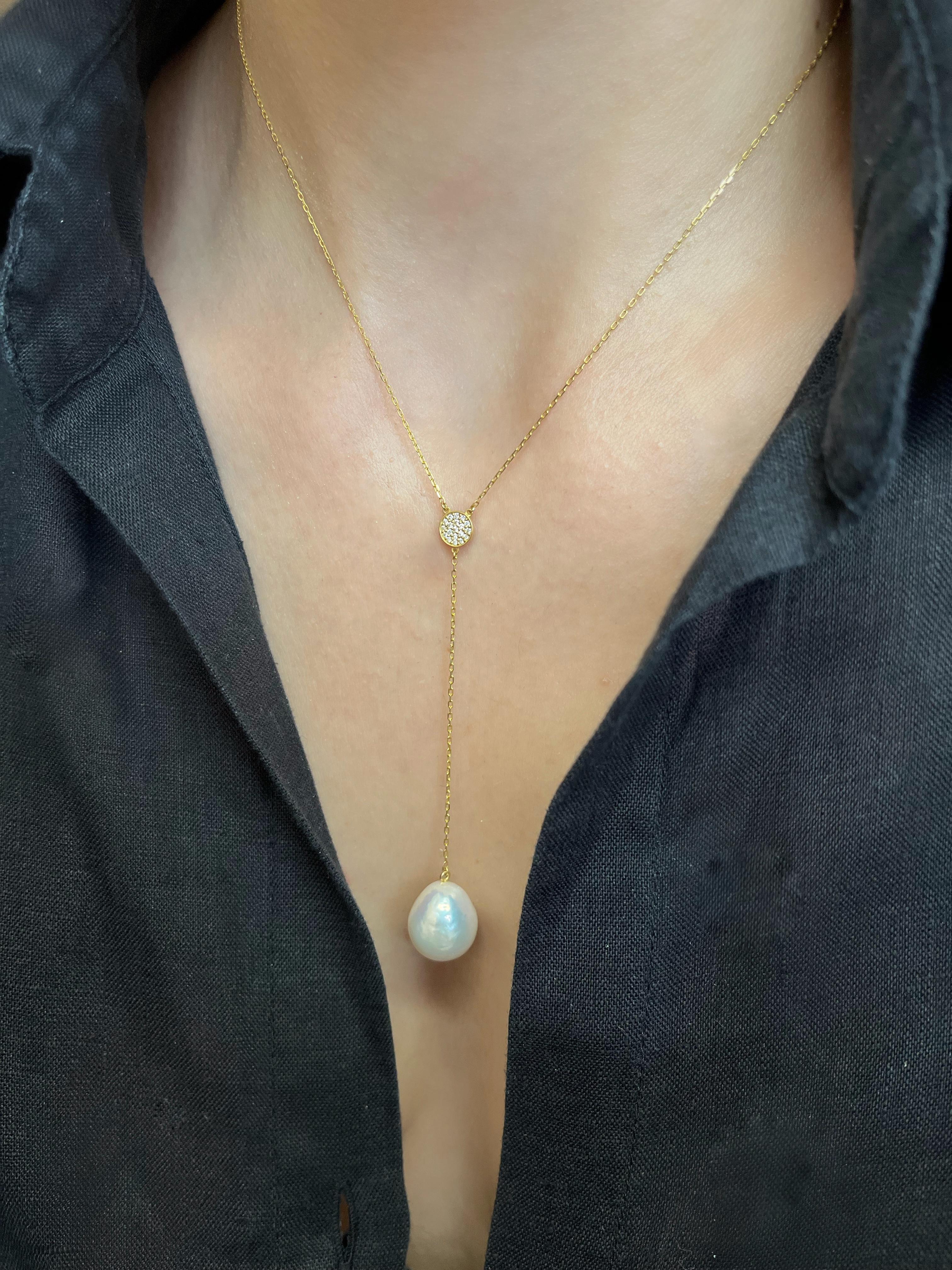 Our lariat necklace features a baroque drop shaped pearl suspended from a sparkly chain and accentuated by a yellow gold disk set with glimmering diamonds.

 The simplicity in its silhouette combined with the high-quality materials used, make this