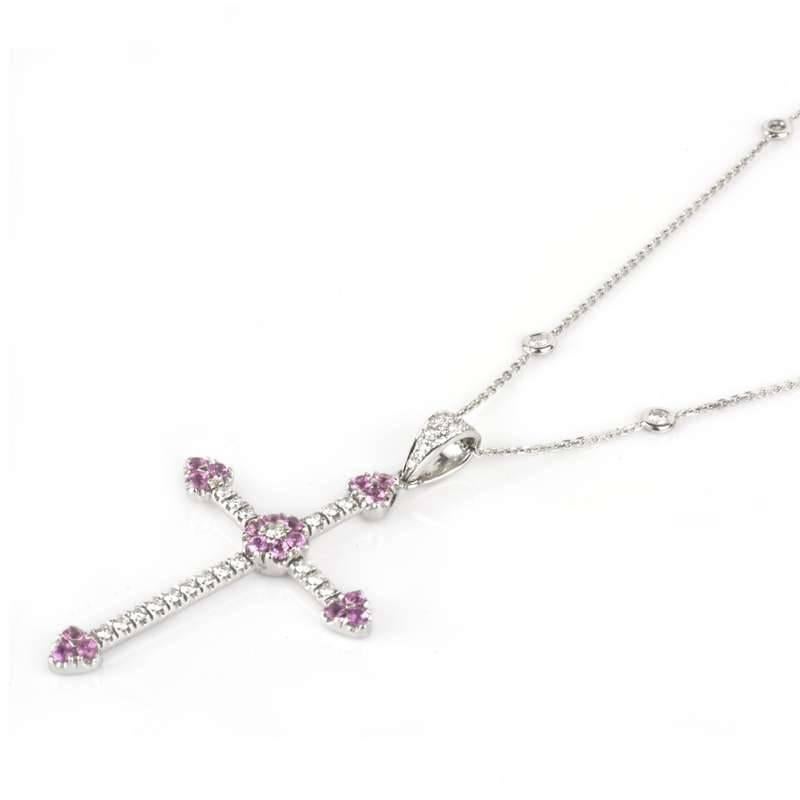 An 18k white gold diamond and pink sapphire cross pendant. The pendant and diamond set bale is set with a total of 27 round brilliant cut diamonds totalling approximately 1.10ct. A further 8 diamonds are spectacle set in the 16'' chain totalling