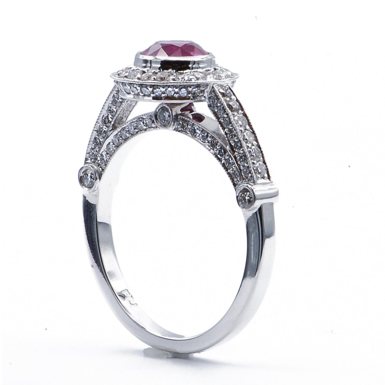 A stunning 18k white gold ring has a vibrant round 1.35 carat Pink Sapphire in the center with a pavé halo.  A row of pavé goes down the sides of the ring on all three side  and across the bridge.  There is an added touch with bezel set stones on