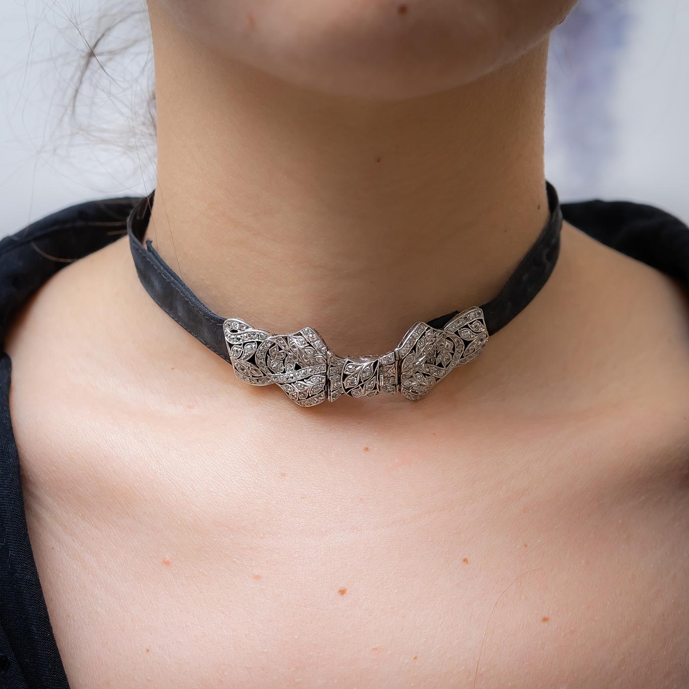 An Art Deco diamond set platinum bow choker, with an old-cut diamond set plaque, in the form of a bow, mounted in platinum, on a black moiré ribbon choker, with an estimated total diamond weight of 1.50ct, circa 1930.

Plaque 68mm, Choker