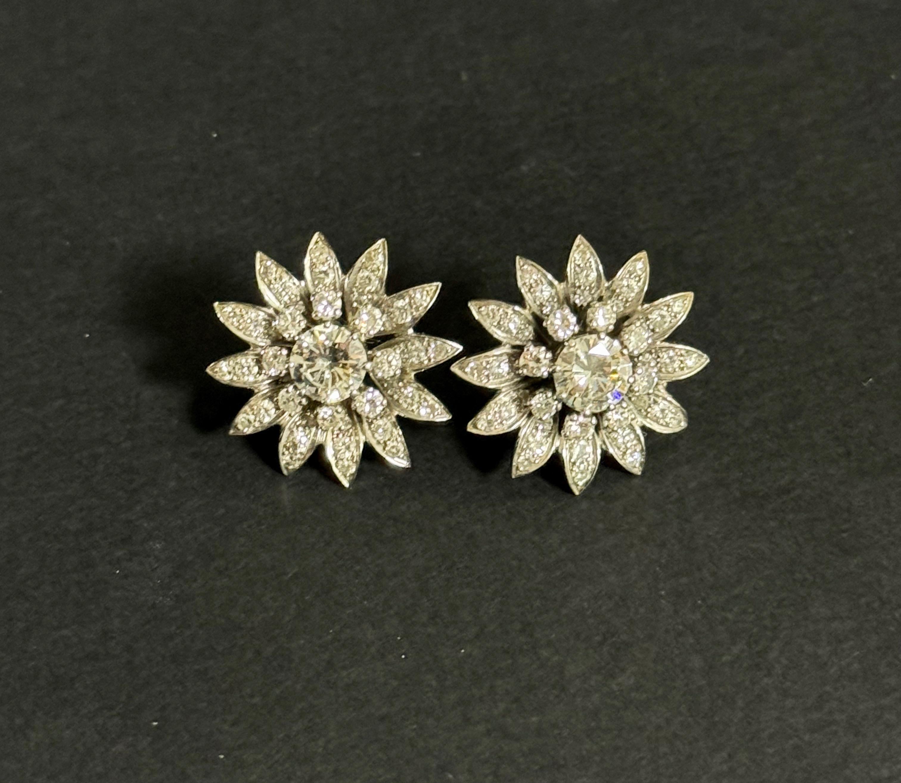 Par de pendientes flor de diamantes, oro blanco y platino. Los pendientes son de hacia 1960. Los diamantes redondos del centro son de talla moderna con tono blanco VSI. Miden alrededor de 1,30 quilates cada una. 
Están rodeados de unos 2,40 quilates