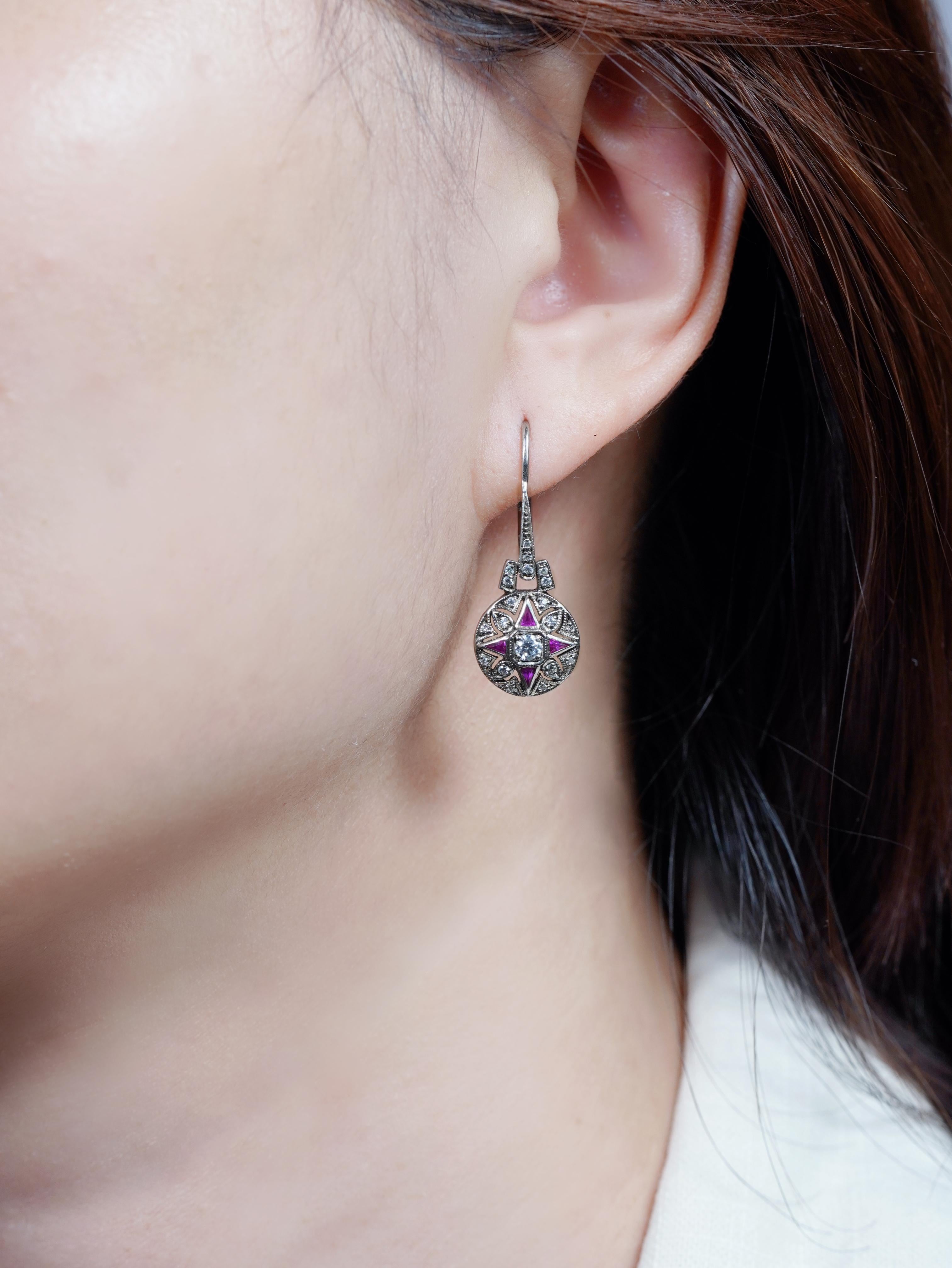 L'élégance intemporelle rencontre le charme vintage dans ces boucles d'oreilles pendantes de style antique. Au centre se trouve un diamant rond brillant, entouré de riches rubis de taille française en forme de triangle qui forment un motif floral
