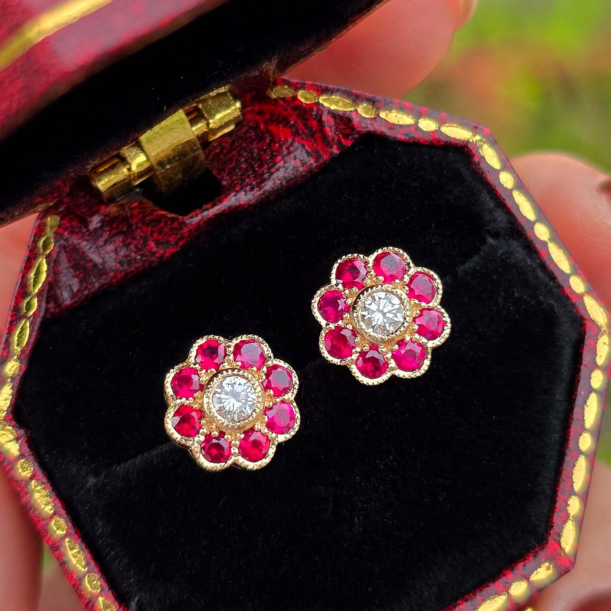 Ces élégantes boucles d'oreilles d'inspiration Art déco présentent un diamant rond au centre, symbolisant l'étamine d'une fleur, entouré de rubis vibrants qui enveloppent délicatement le diamant comme de délicats pétales. L'association de diamants