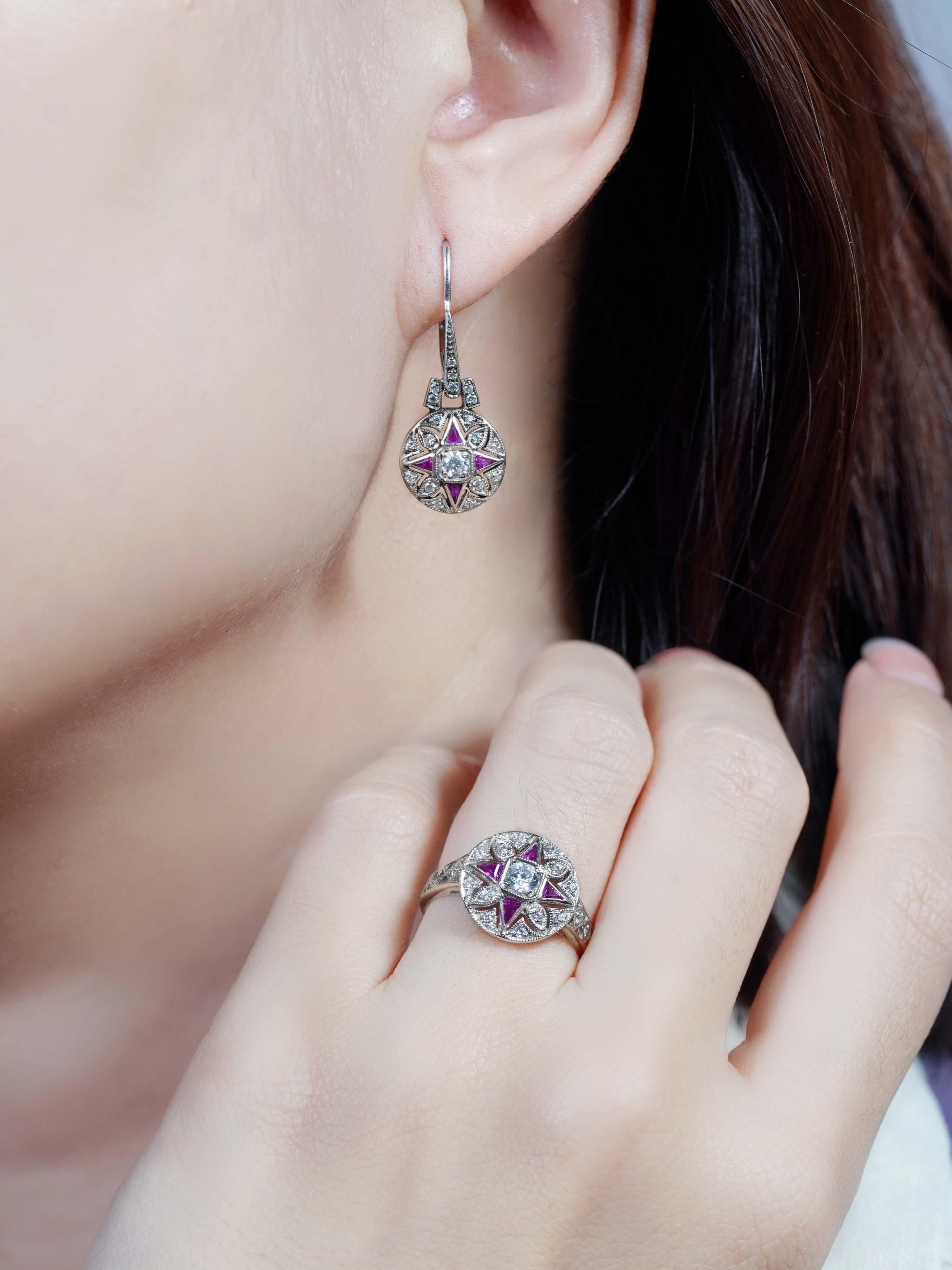 A beautifully coordinated ring and earrings, each centered with a round brilliant diamond. Surrounding the center stone are vivid, triangle-cut rubies set to the left, right, top, and bottom—forming a bold, geometric floral motif. The ring’s