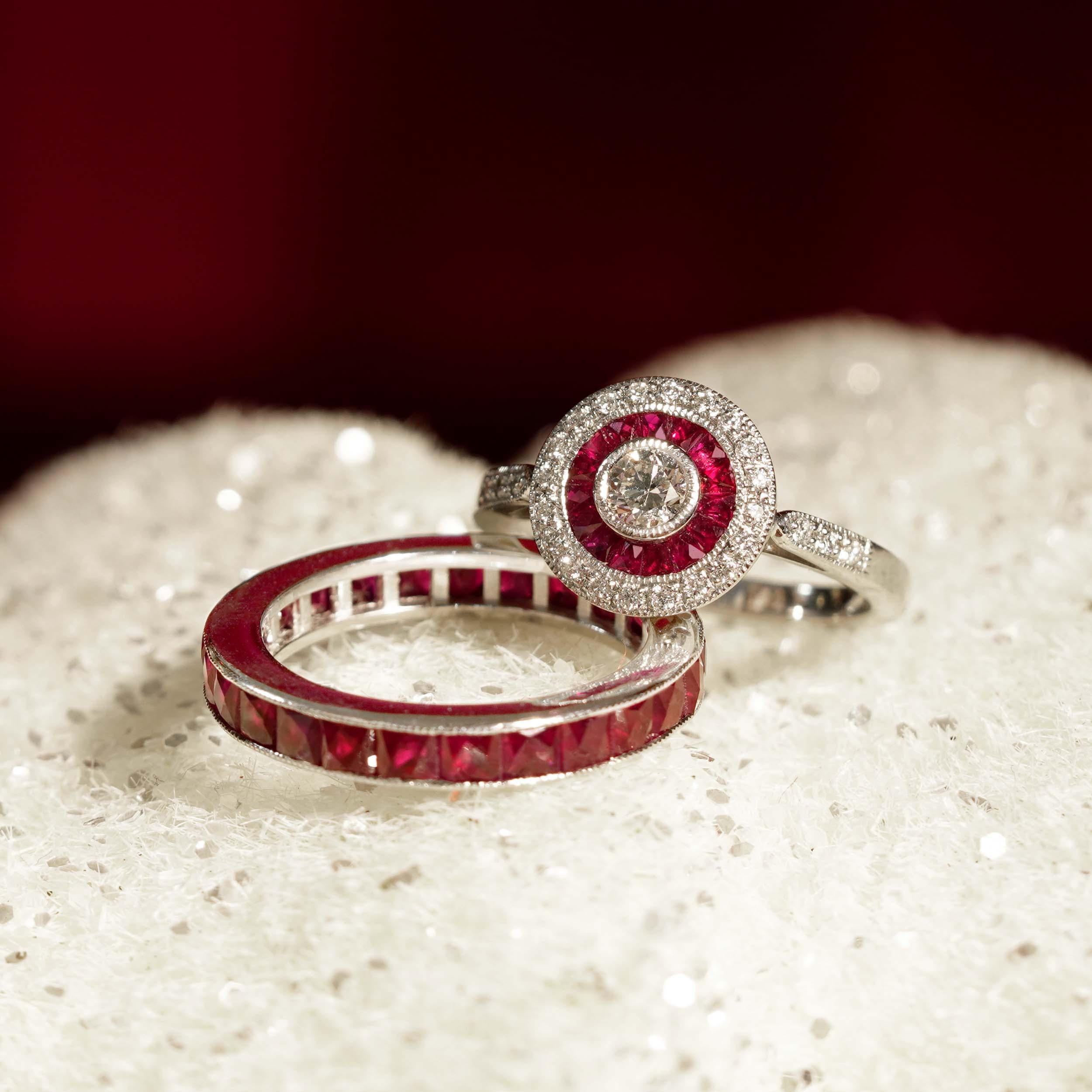 This Diamond and Ruby Art Deco Style Target Engagement Ring showcases a brilliant round diamond at its center, surrounded by a vibrant of rich rubies, and further encircled by sparkling diamonds. The striking Art Deco design blends bold geometry