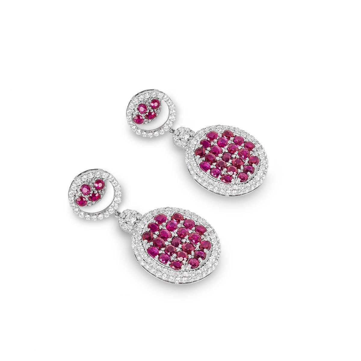 An 18k white gold pair of diamond and ruby earrings. The earrings feature two circular motifs suspended from one another set with pave round brilliant cut diamonds through the outer edge with round rubies set in the centre. The diamonds have a