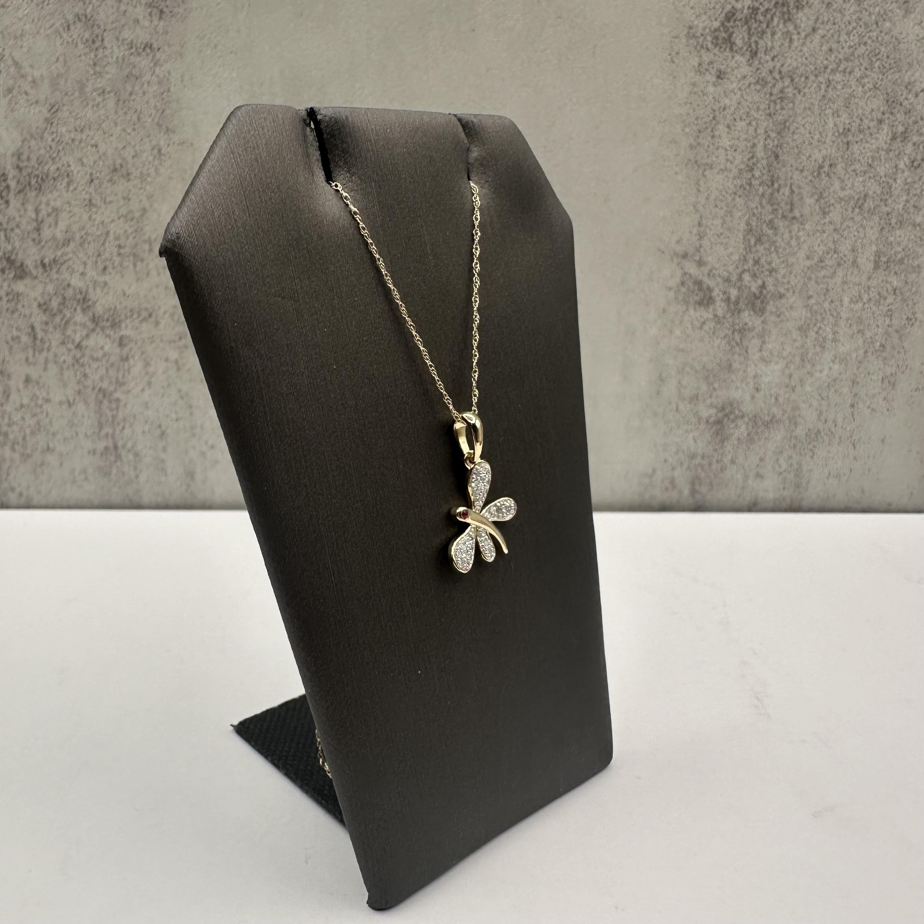 Verleihen Sie Ihrer Kollektion einen skurrilen und eleganten Touch mit dieser Libellen-Halskette mit Diamanten und Rubinen, die aus 10kt Gelbgold gefertigt ist. Dieses zarte Libellendesign mit 0,15 Karat Gesamtgewicht (ctw) aus natürlichen Diamanten