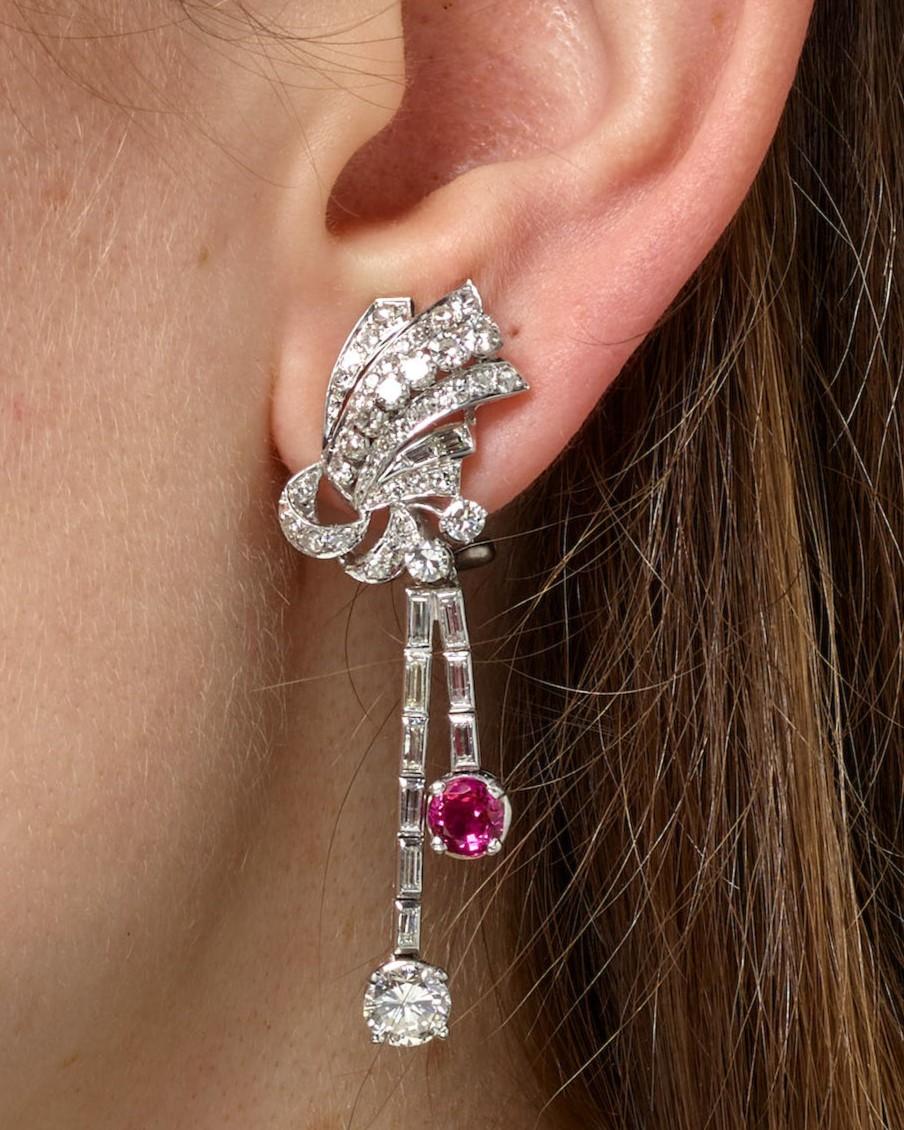 Questi splendidi orecchini sono progettati come nodi stilizzati di diamanti singoli e rotondi con taglio a brillante, ciascuno unito a nappe sospese di diamanti baguette e rotondi con taglio a brillante, per finire con un unico rubino con taglio