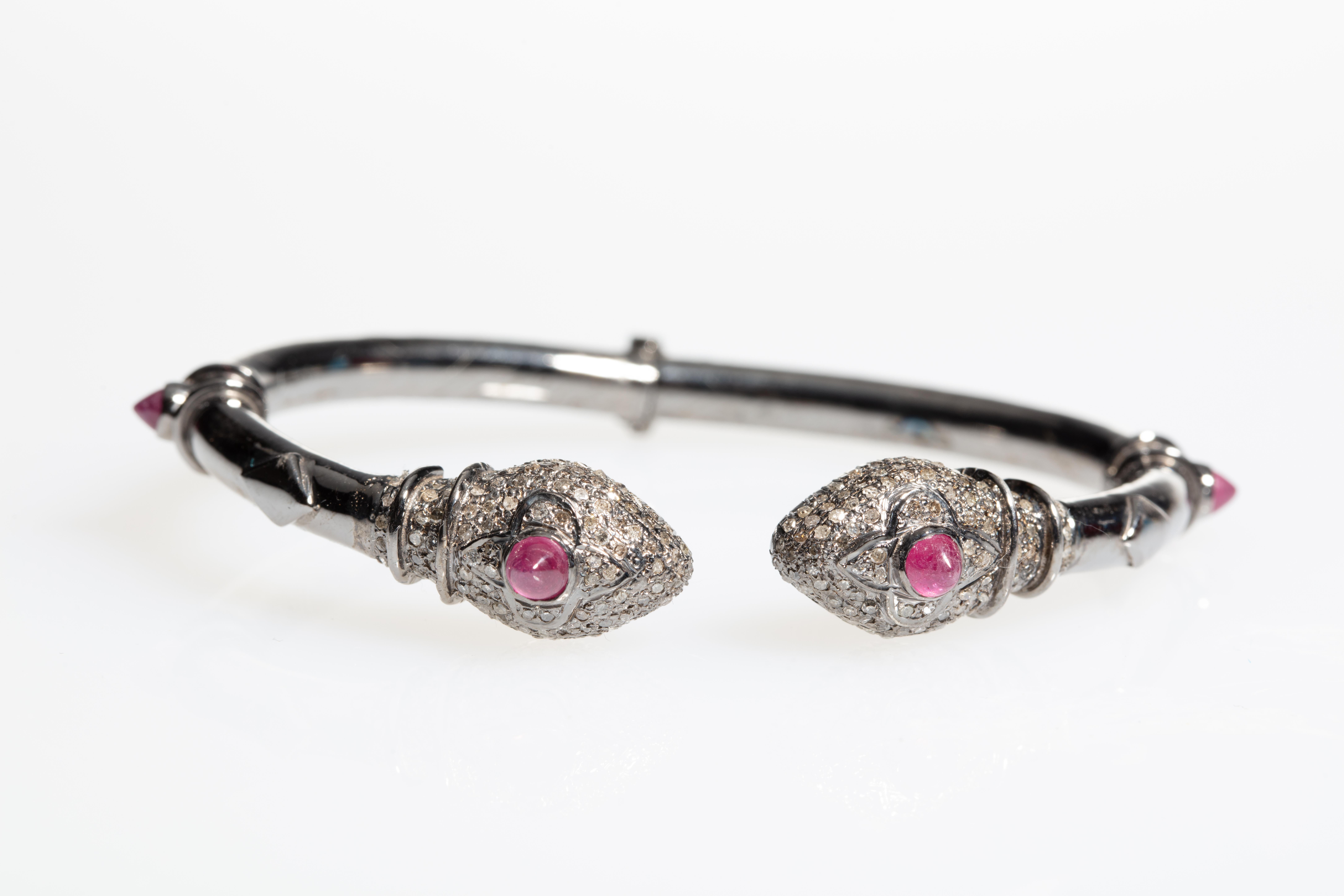A double-headed snake bracelet with pave-set diamonds on the head and beveled Burmese ruby third eye with rubies at the sides as well.  Set in an oxidized sterling silver.  Hinged at the back for easy on and off.  Oval shape to keep the workmanship