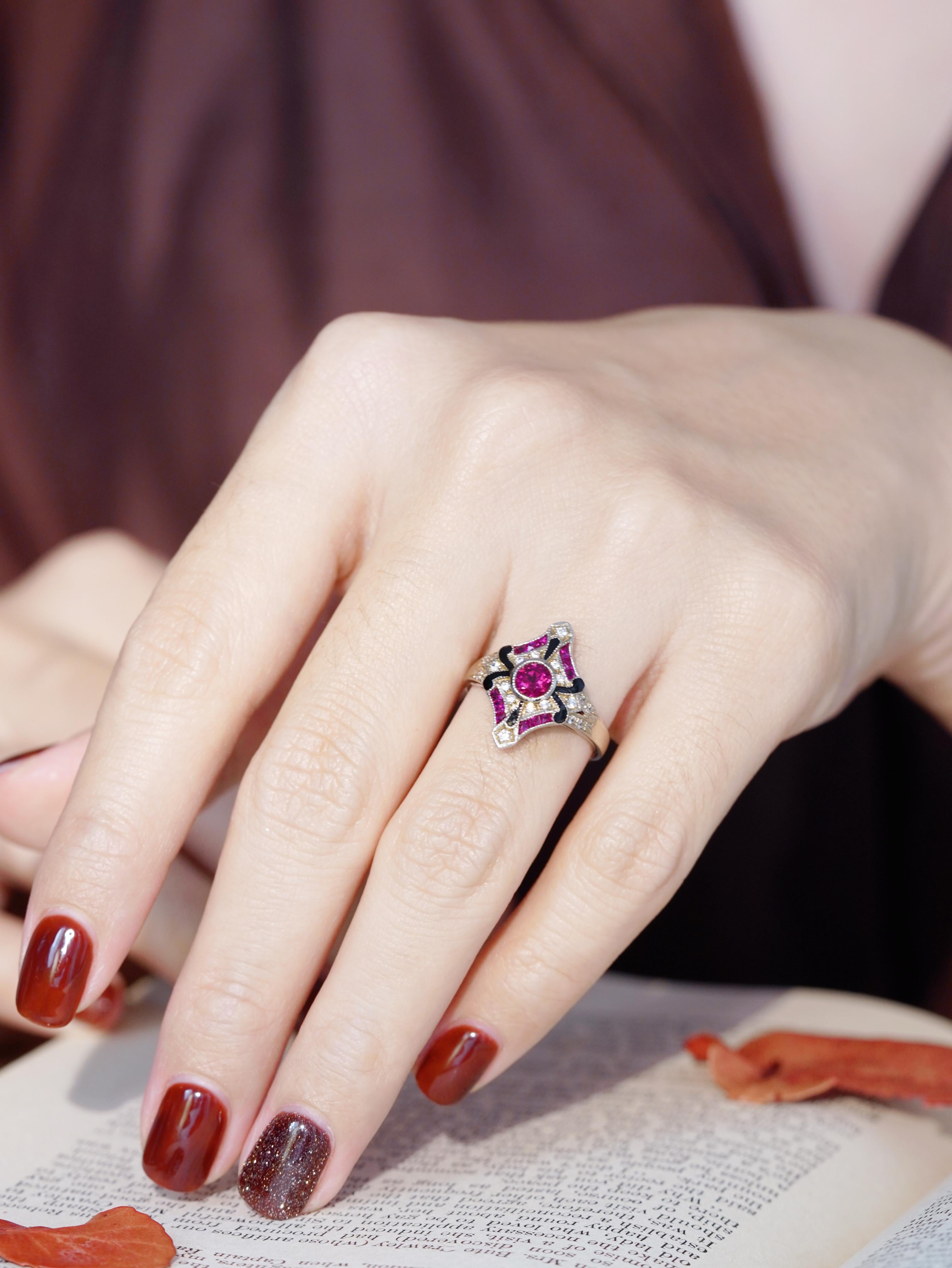 This stunning Art Deco-style ring features a vibrant bezel-set ruby at its center, exuding timeless elegance and sophistication. The intricately contoured frame is adorned with sparkling diamonds and fine enamel detailing, adding depth and vintage