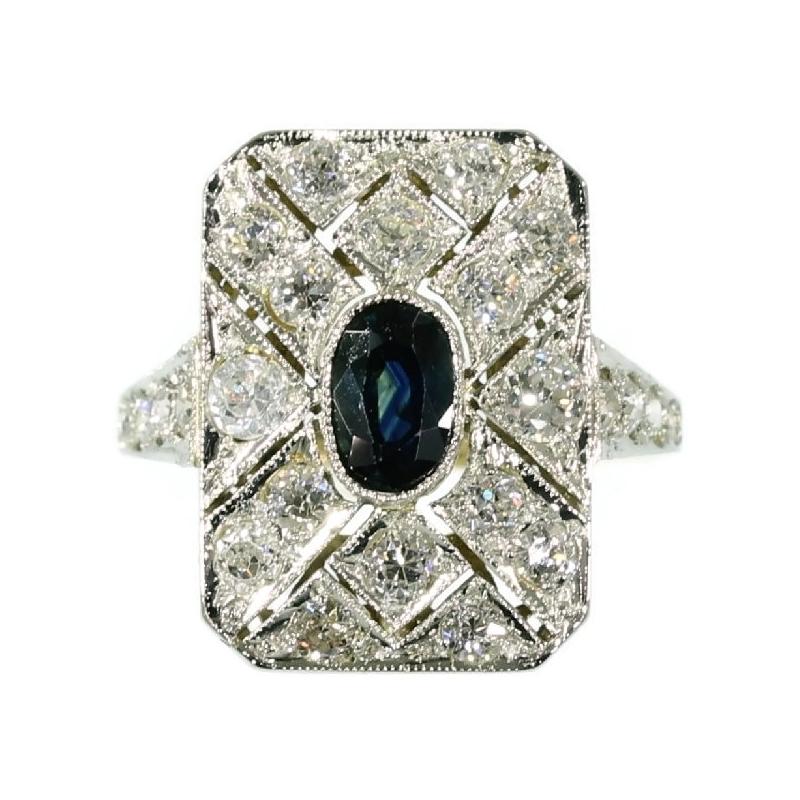 An oval cut sapphire encrusted in the intersection of the pierced diagonals of this 18K yellow gold rectangular ring from 1920 enhances this jewel into an authentic Art Deco emblem. Its geometrically pierced cadre with 16 old European cut diamonds