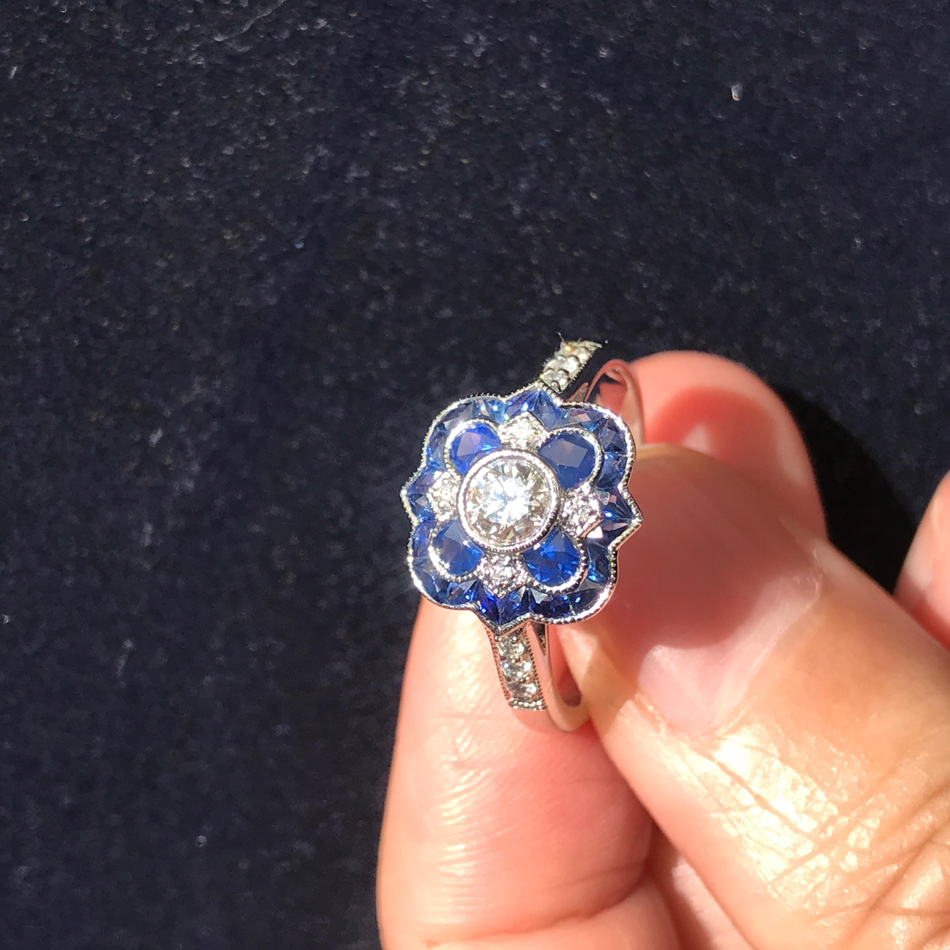 Questo splendido anello in stile Art Déco si ispira alla bellezza di un fiore che sboccia. Al centro si trova un diamante rotondo che rappresenta il pistillo e che irradia brillantezza e purezza. Attorno ad esso ci sono strati di ricchi zaffiri blu,