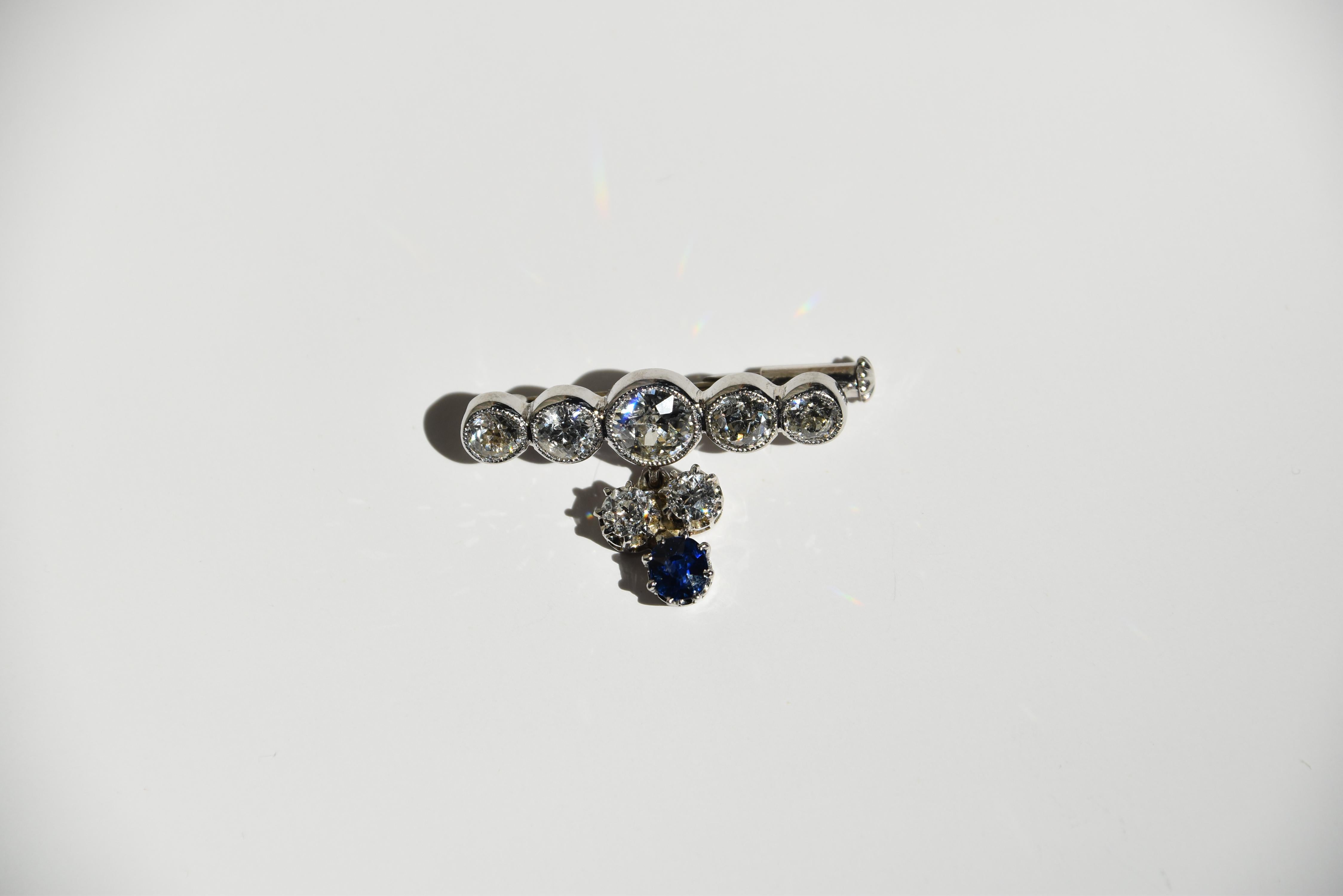 A diamond and Sapphire brooch, designed as a millegrain set old brilliant cut diamond graduated five stone bar, the central diamond weighing approximately 0.50 carats, suspending a sapphire and diamond three stone drop

length: 2.6cm
Date: