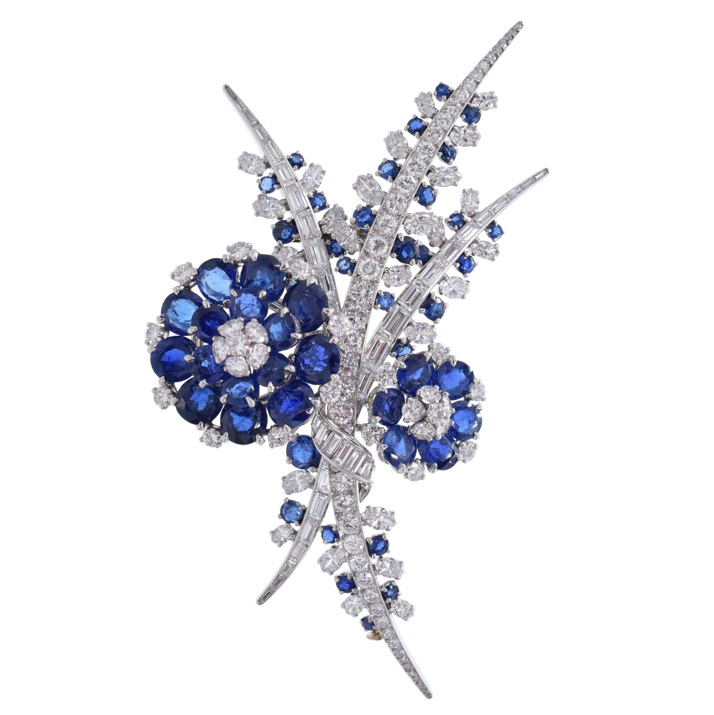 Diamond and Sapphire Flower Brooch, French This
brooch has a two flowers motif with stylistic foliage of
round brilliant, marquise, baguette, and single cut diamonds weighing approximately 10ct total, and oval and round faceted sapphires