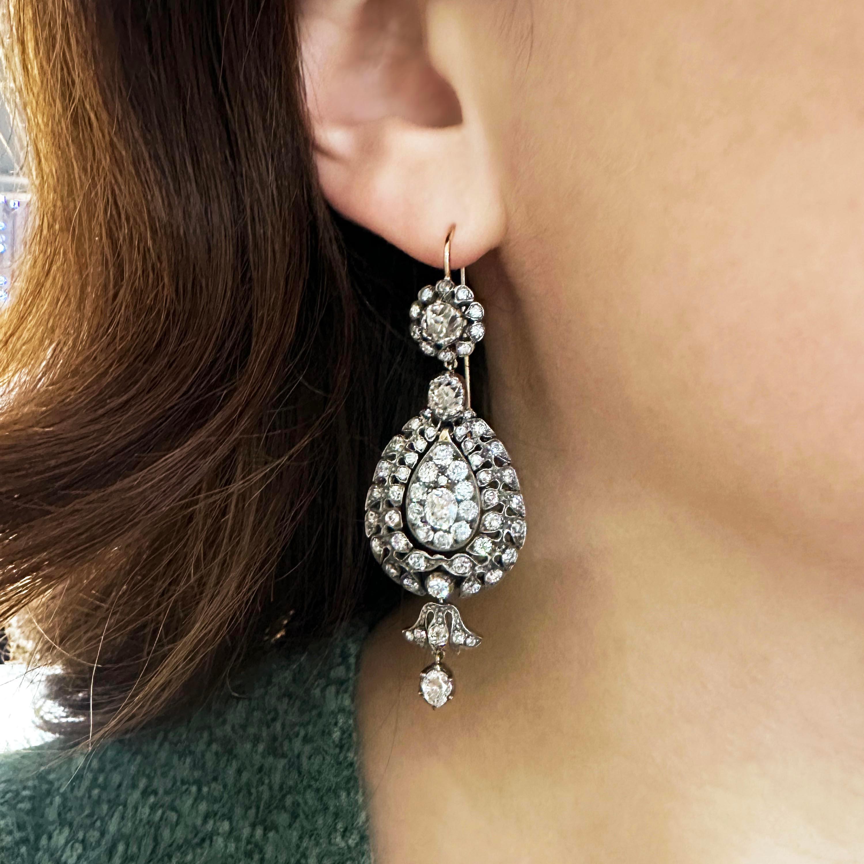 A pair of antique style, diamond set, drop-shape earrings, with a cluster at the top and a pendant, hanging from the bottom of the drop, set with approximately 10.38ct of cushion, oval and round old-cut diamonds, mounted in silver-upon-gold, on hook