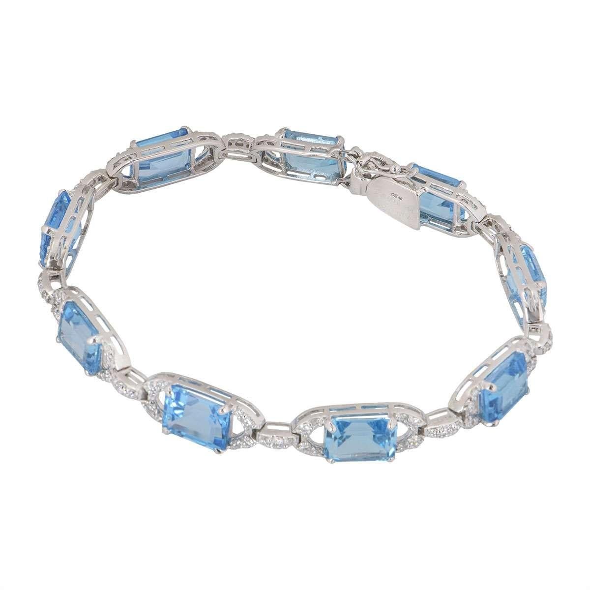 An 18k white gold diamond and topaz bracelet. The bracelet is set with 9 emerald shaped topaz stones which are complemented by round brilliant cut diamonds on the conjoining mounts. The topaz has a total weight of 19.50ct and the diamonds total