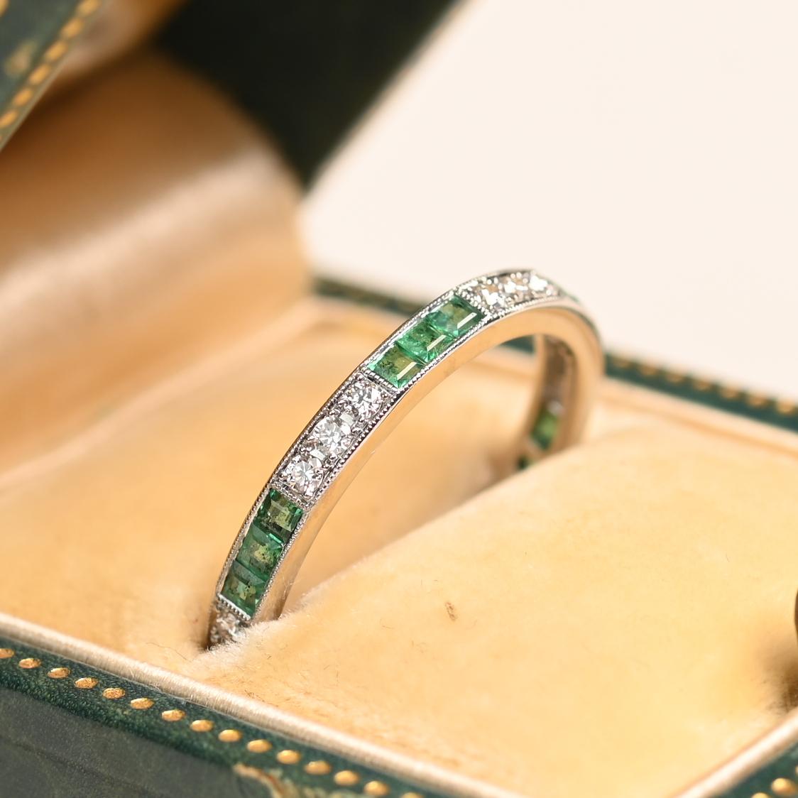 Cette alliance raffinée de style Eleg présente une élégante alternance d'émeraudes de taille calibre serties en canal et de diamants ronds de taille brillant sertis en pavé. Les pierres sont encadrées de délicats détails de milgrain, ajoutant une
