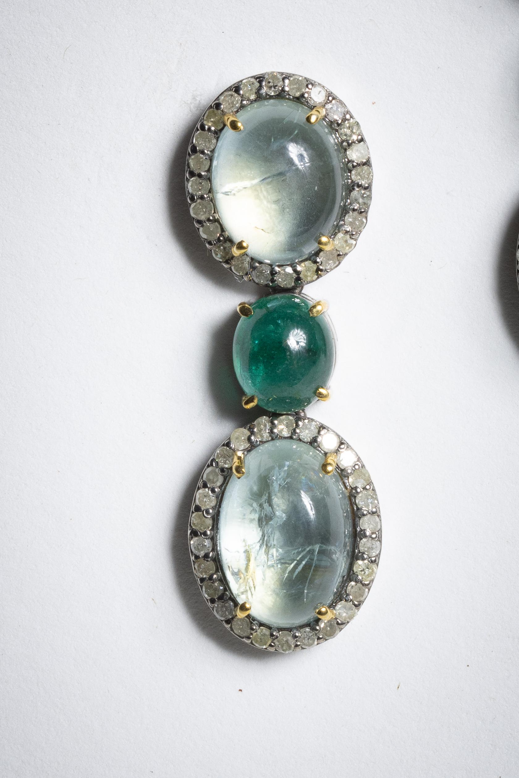 A classic and yet unusual double drop pair of earrings featuring oval cabochon aquamarines with an oval, cabochon emerald in between.  The aquamarines are bordered in pave`-set, round, brilliant cut diamonds.  Set in sterling silver with an 18K gold