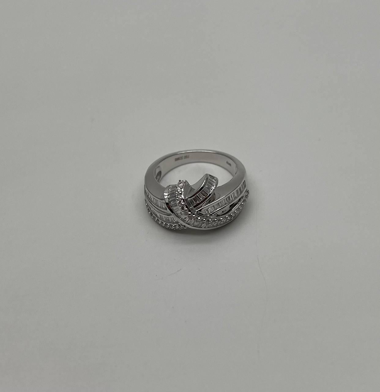 Une touche moderne d'élégance et de forme.
Cette bague remarquable présente un design complexe avec des bandes entrelacées. La tige en métal poli est ornée d'une série de diamants de taille baguette, créant un flux continu d'éclat et de