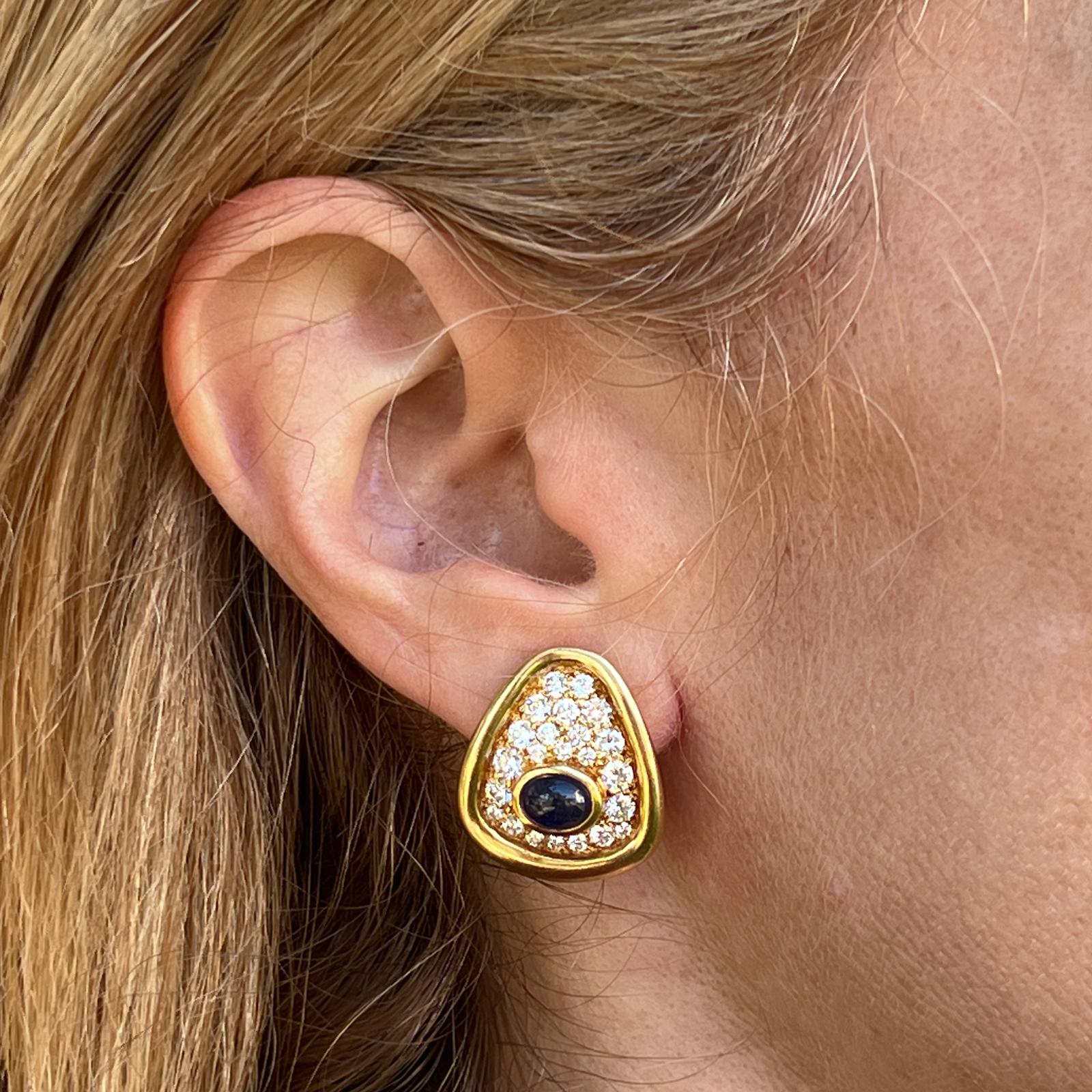Beautiful diamond and sapphire earrings handcrafted in 18 karat yellow gold. The earrings feature 46 round brilliant cut diamonds weighing approximately 2.00 carat total weight, and two cabochon blue sapphires weighing approximately 2.40 CTW. The