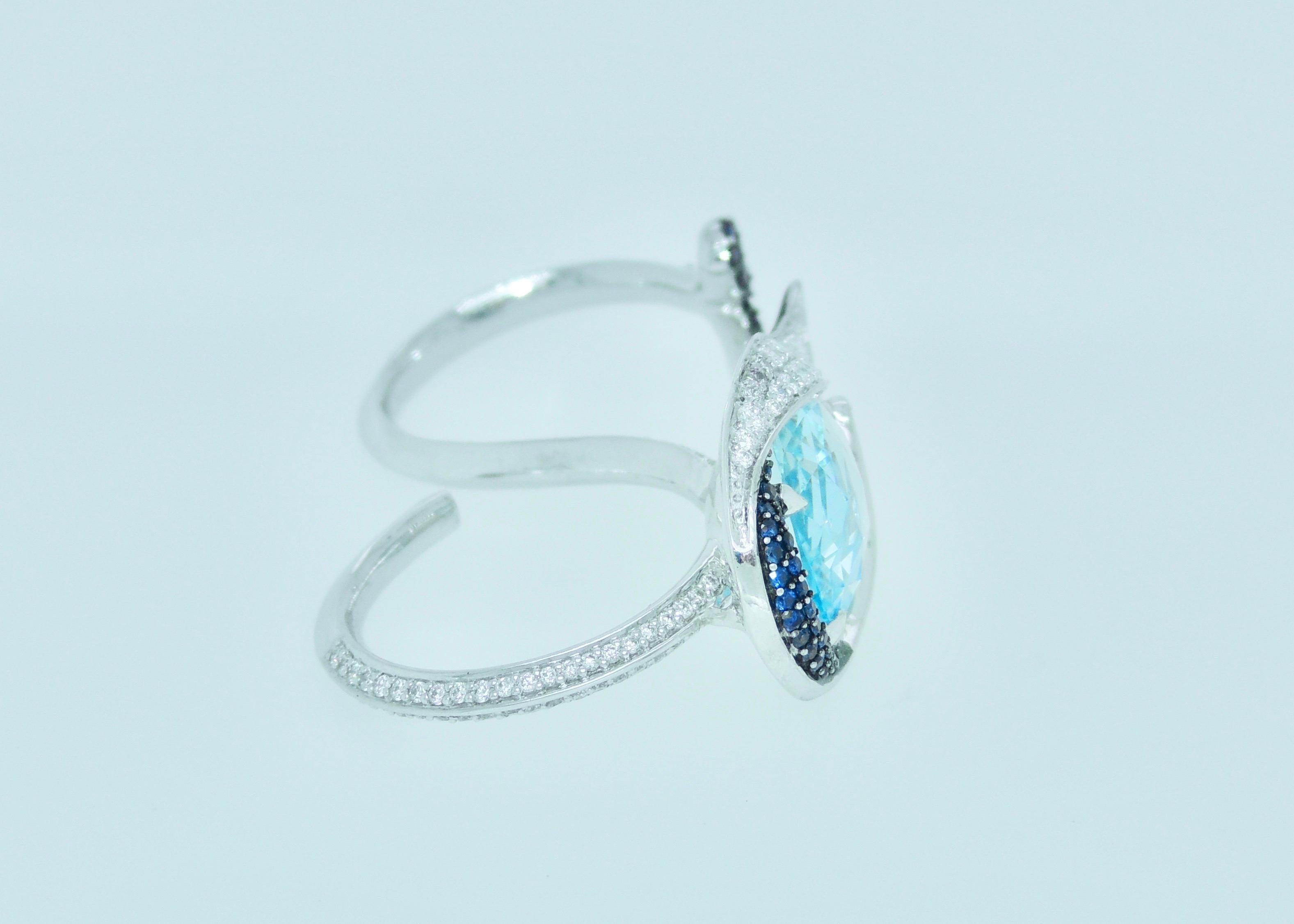 A beautiful, rare faceted oval aquamarine is set in this two finger earring with diamonds and blue sapphire. The design is inspired by the swirl like waves in the ocean that create so many different hues of blue. 
The light blue of the aquamarine