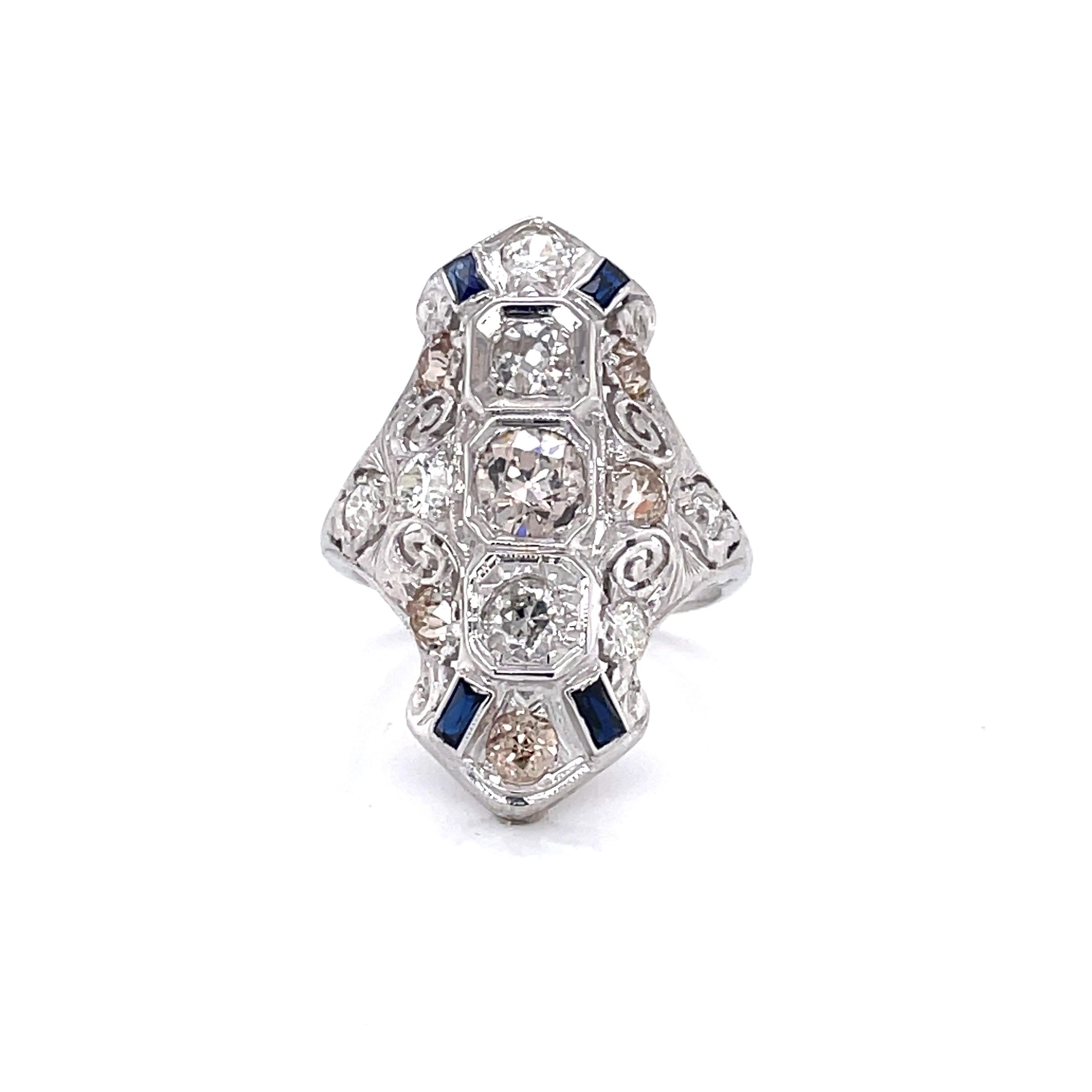 Twelve white hand cut Miner's cut diamonds with total weight of 1.25 carats are artfully set in fancy fourteen karat 14K white gold filigree with blue sapphire accents.
This larger profile Edwardian ring measures approximately 28mm long and 18mm in