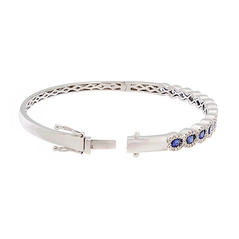 13 round cut graduating blue sapphires totaling 1.76 carats run half circle around this bracelet. With 0.62 carats of diamonds, each sapphire has an oval shape halo of diamonds. The bracelet is set in 18K white gold with a box clasp closure and a