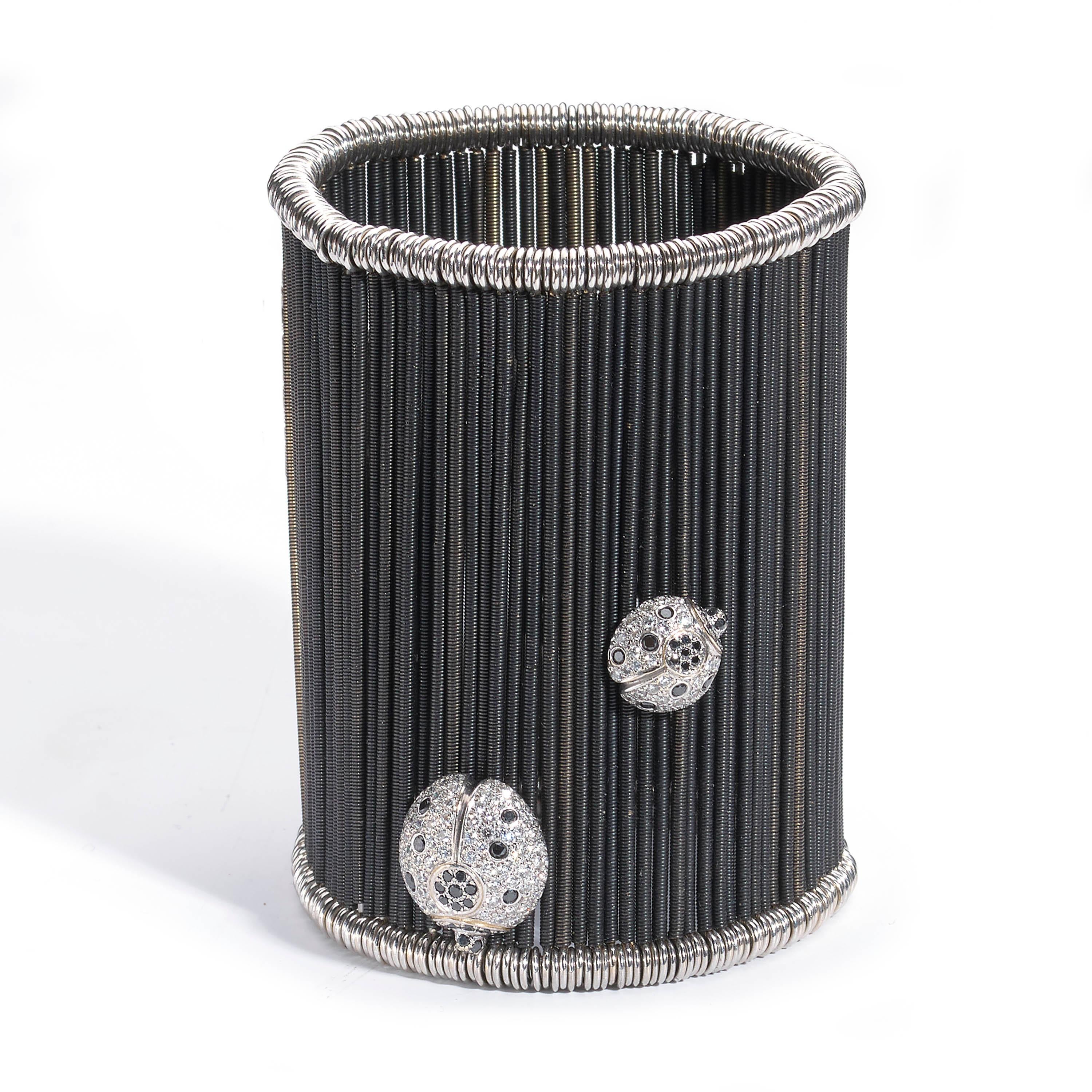 A modern cuff bracelet, comprised of anodised white gold twisted bars, on sprung fittings, with a large white and black brilliant-cut diamond-set butterfly applied to the front, with two smaller ladybirds applied to the reverse, also set with white