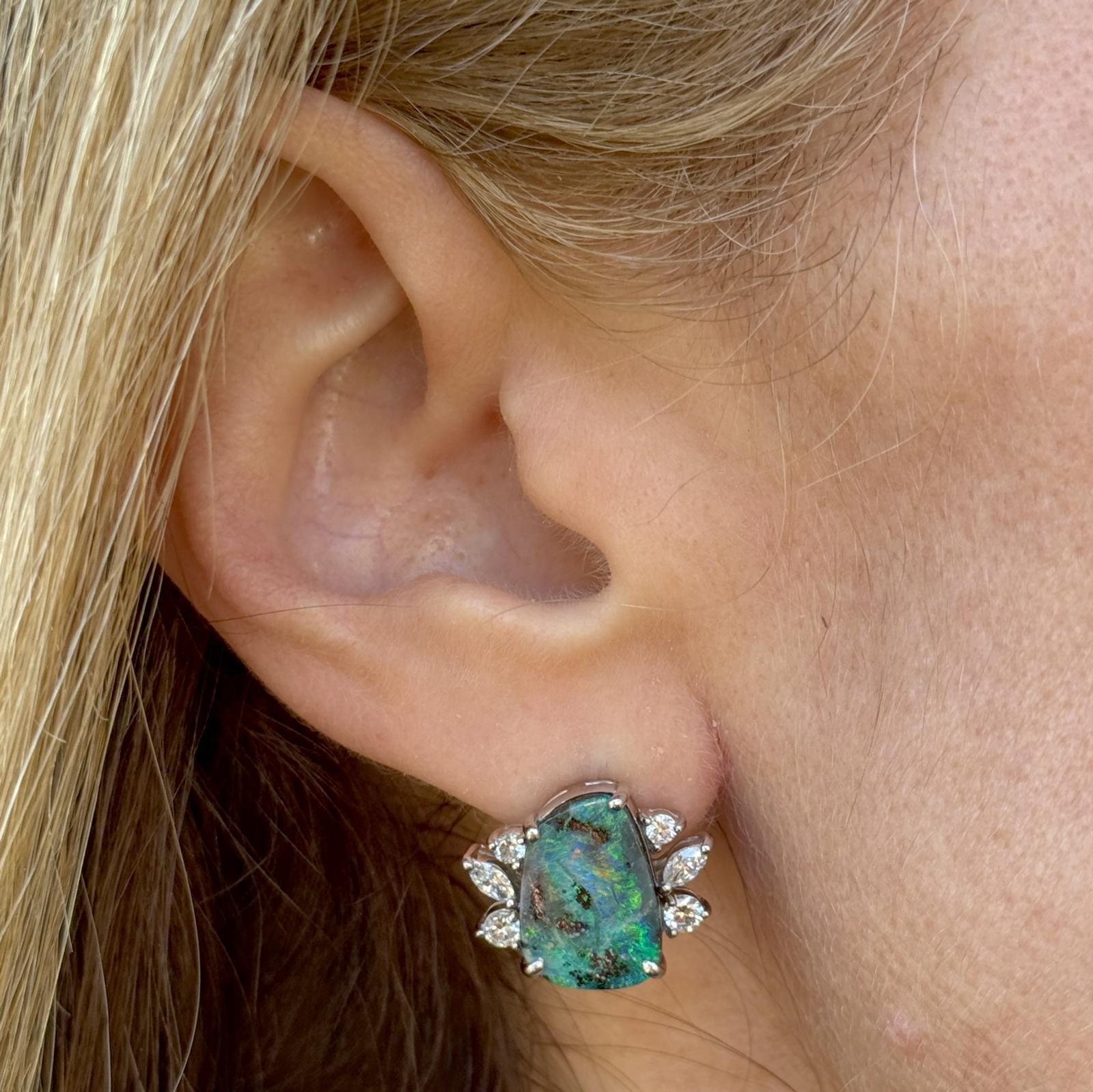 These exquisite 14 karat white gold diamond and opal earrings combine classic elegance with a touch of vibrant color. Each earring features a luminous opal center stone, radiating captivating flashes of blue and green color. Surrounding the opals
