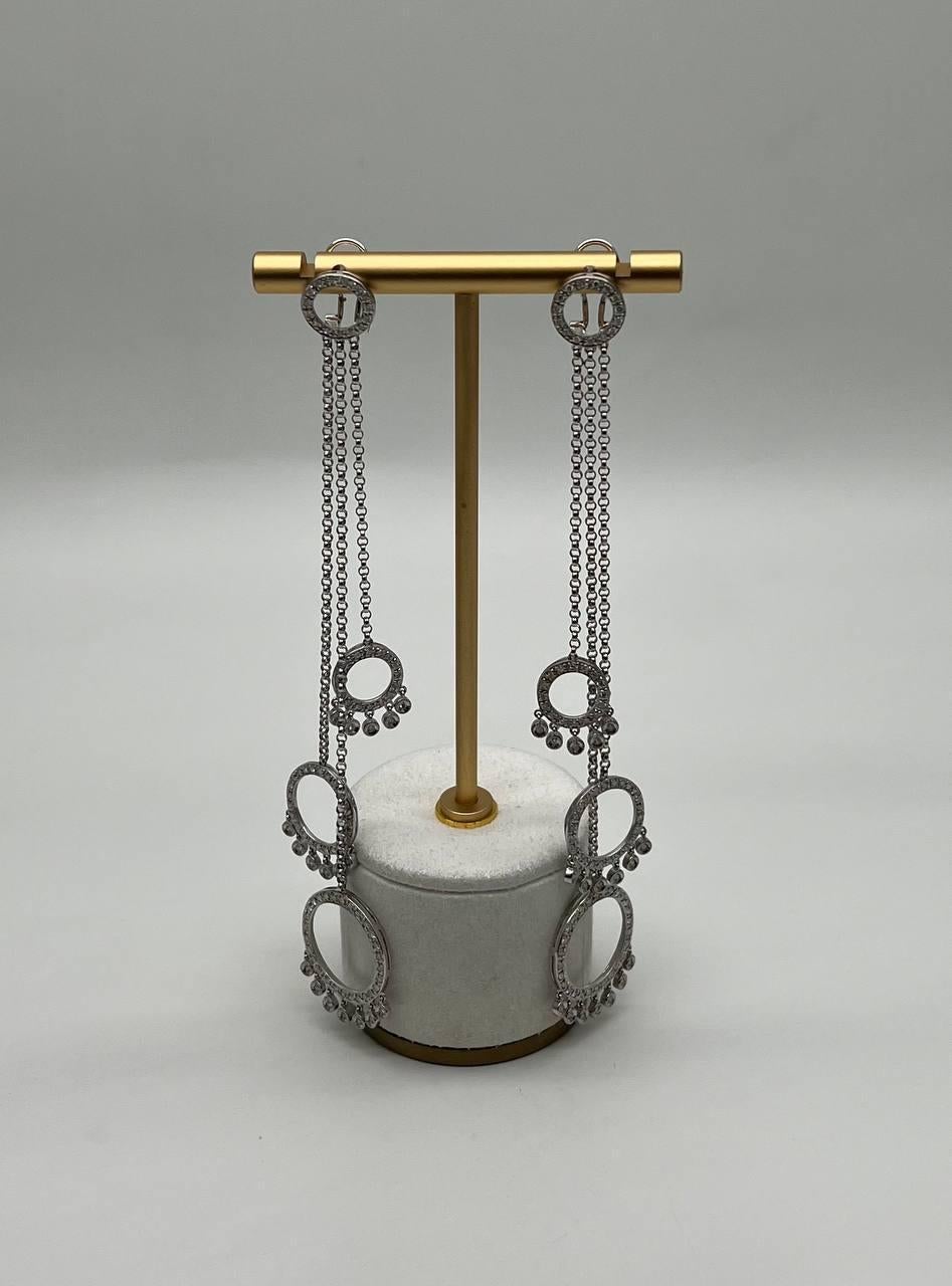 These striking earrings feature a unique design with elongated, articulated metal strands. Each strand is adorned with circular and gear-like shapes, creating an industrial aesthetic. The metal has a polished finish, enhancing the intricate details