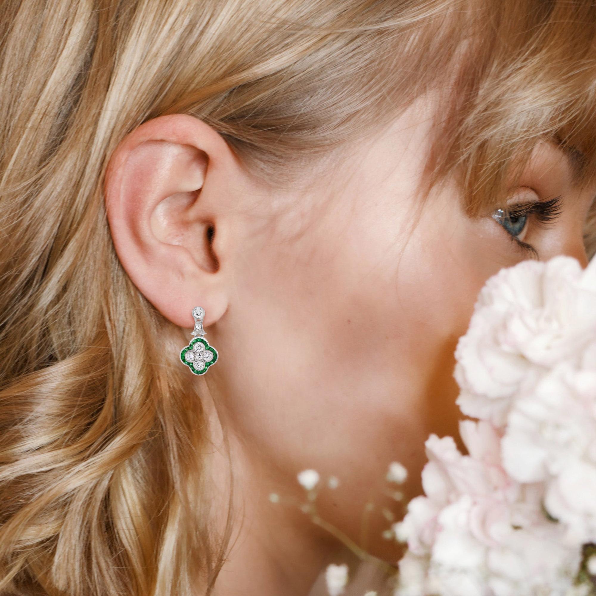 These captivating Art Deco-style floral earrings feature a stunning blend of vibrant emeralds and sparkling diamonds. The intricate floral design showcases the brilliance of the diamonds cluster, surrounded by a halo of radiant French cut emeralds