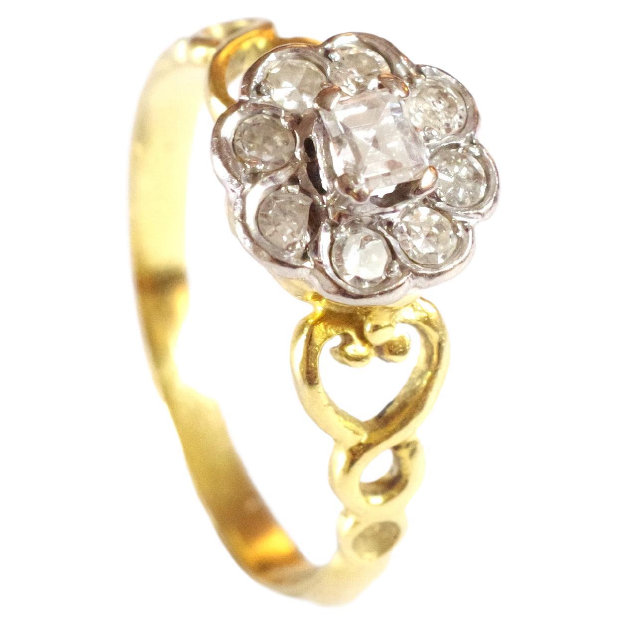 Diamond cluster flower ring in 18 karats white and yellow gold. A central fantasy cut diamond of rectangular shape is surrounded by eight old single cut and brilliant cut diamonds in a white gold setting. The ring takes the shape of a flower. The
