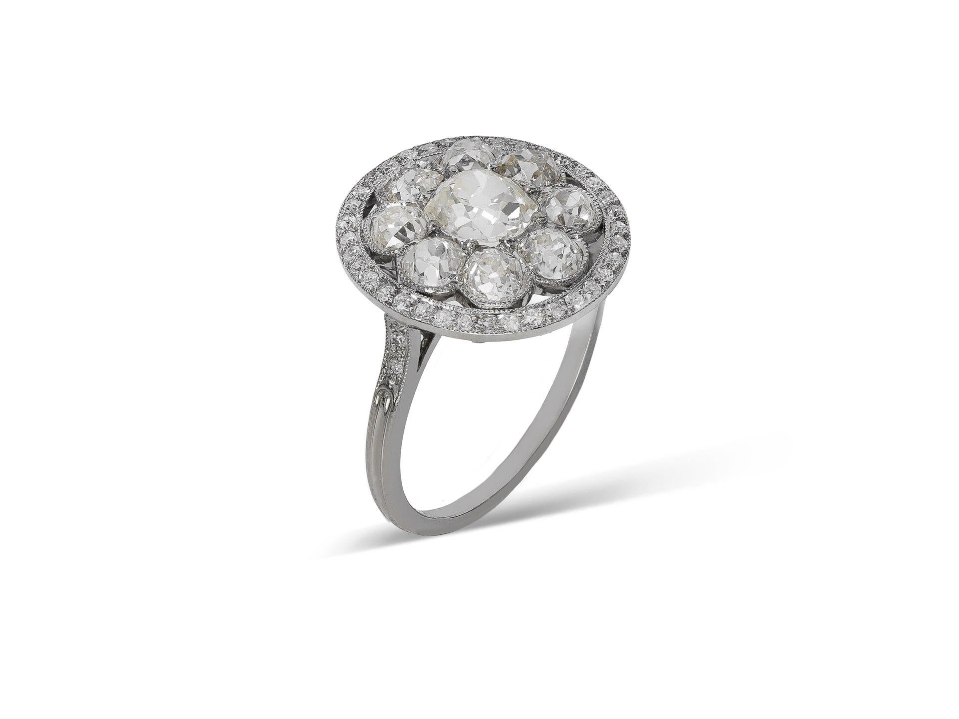 Diamond cluster ring. Set to centre with a cushion shape old mine diamond in an open back claw setting with an approximate weight of 0.80 carats, encircled by eight cushion shape old mine diamonds in open back grain and rubover settings with a