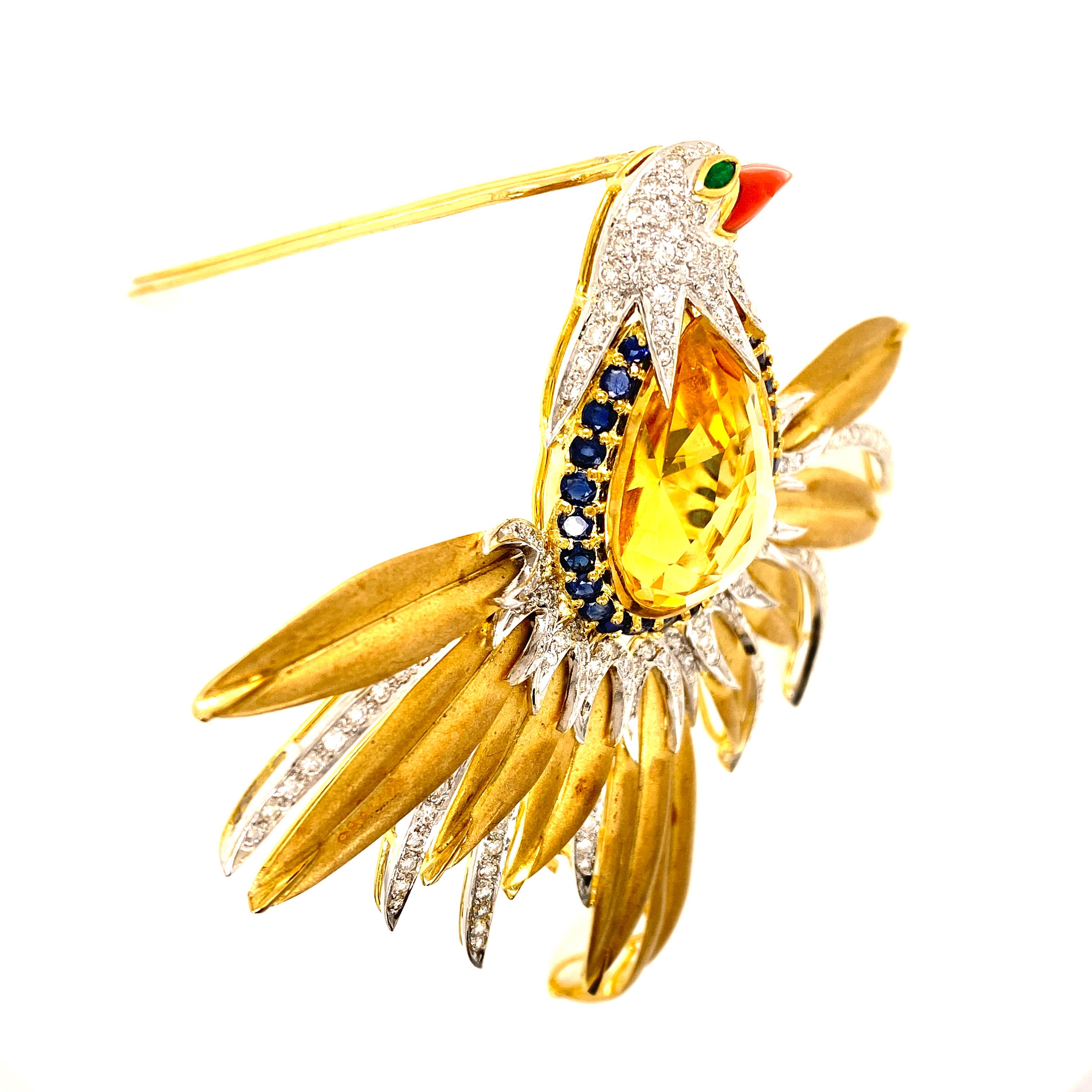 Beautiful Statement Bird Brooch fashioned in 18 karat yellow gold. This piece of art features a 26.75 carat faceted citrine gemstone as the body of the bird surrounded by sapphires, diamonds, emerald, and coral accents. The wings span 3.5 inches in