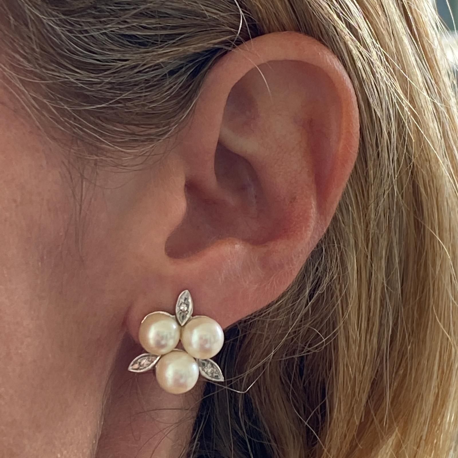 Diamond and pearl floral motif earrings are fashioned in 14 karat white gold. The earrings feature 6 cultured 7.5mm pearls and 6 single cut diamonds weighing approximately .06 carat total weight. The earrings measure 20 x 20mm and feature clip backs.