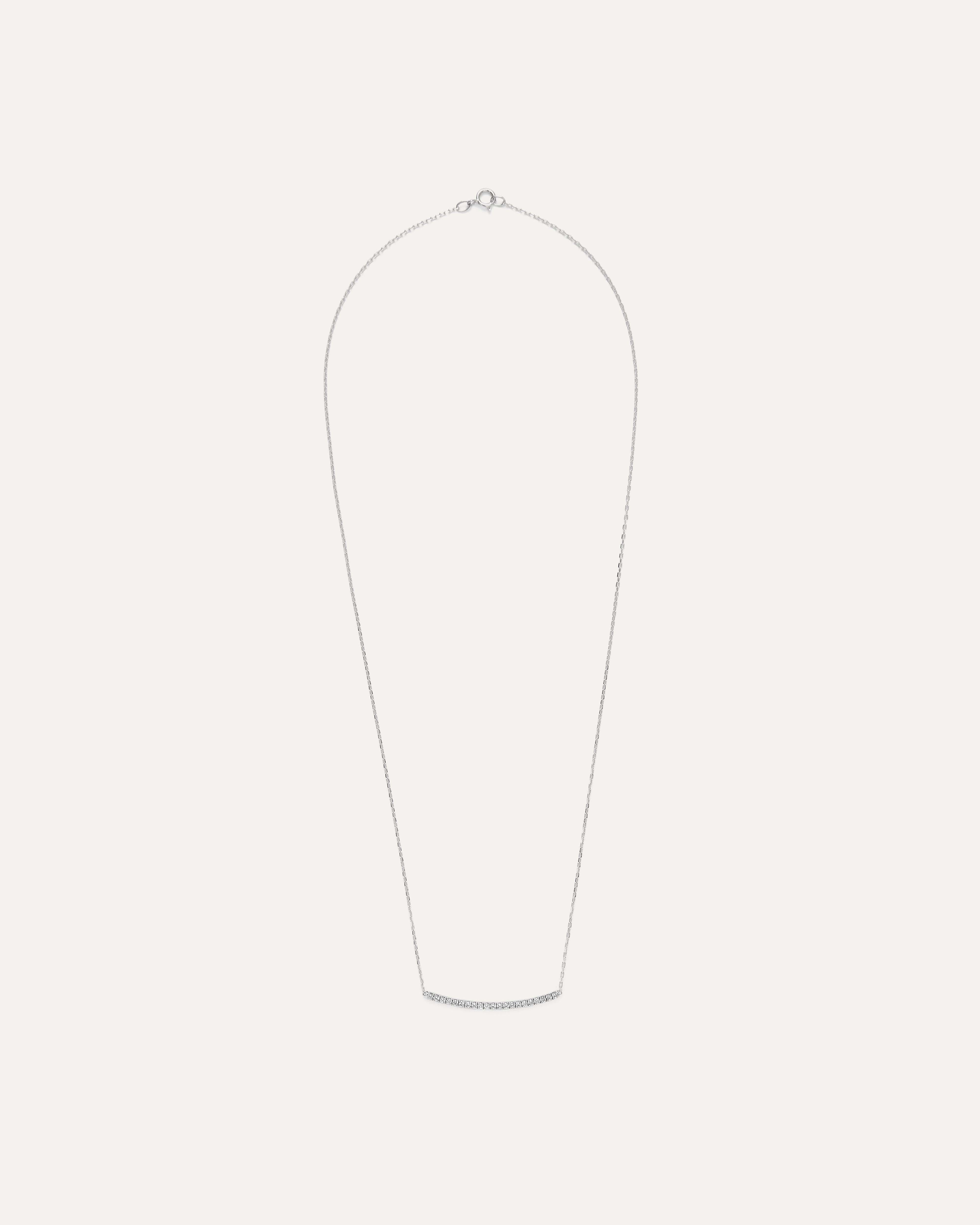 A Diamond Curve Bar Necklace is a striking and contemporary piece of jewelry that seamlessly marries elegance with modern design. This necklace features a gently curving bar, often crafted from white gold or platinum, adorned with a row of exquisite