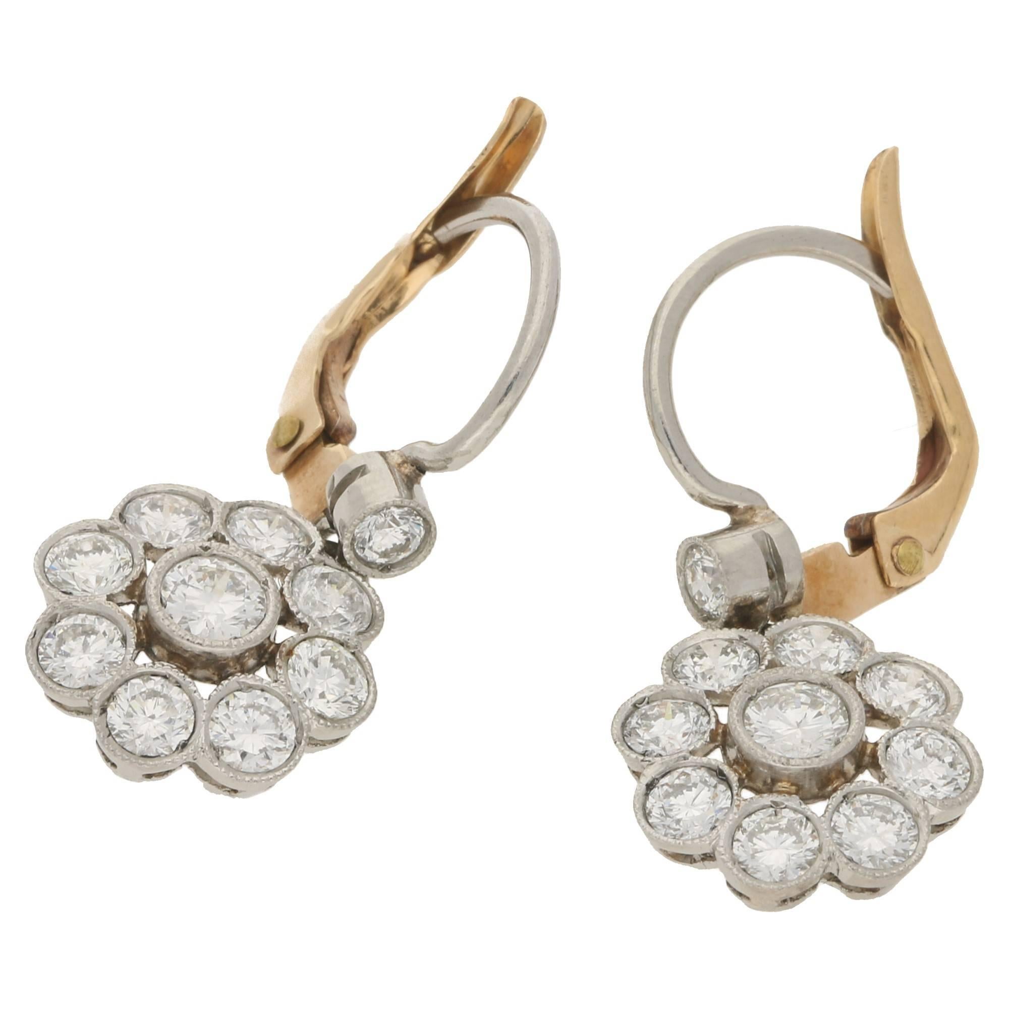 A gorgeous pair of diamond daisy cluster drop earrings. Each earring is formed of a collection of round brilliant cut diamonds forming a daisy motif with one set centrally with eight diamonds forming the outer detail. The diamonds are set in