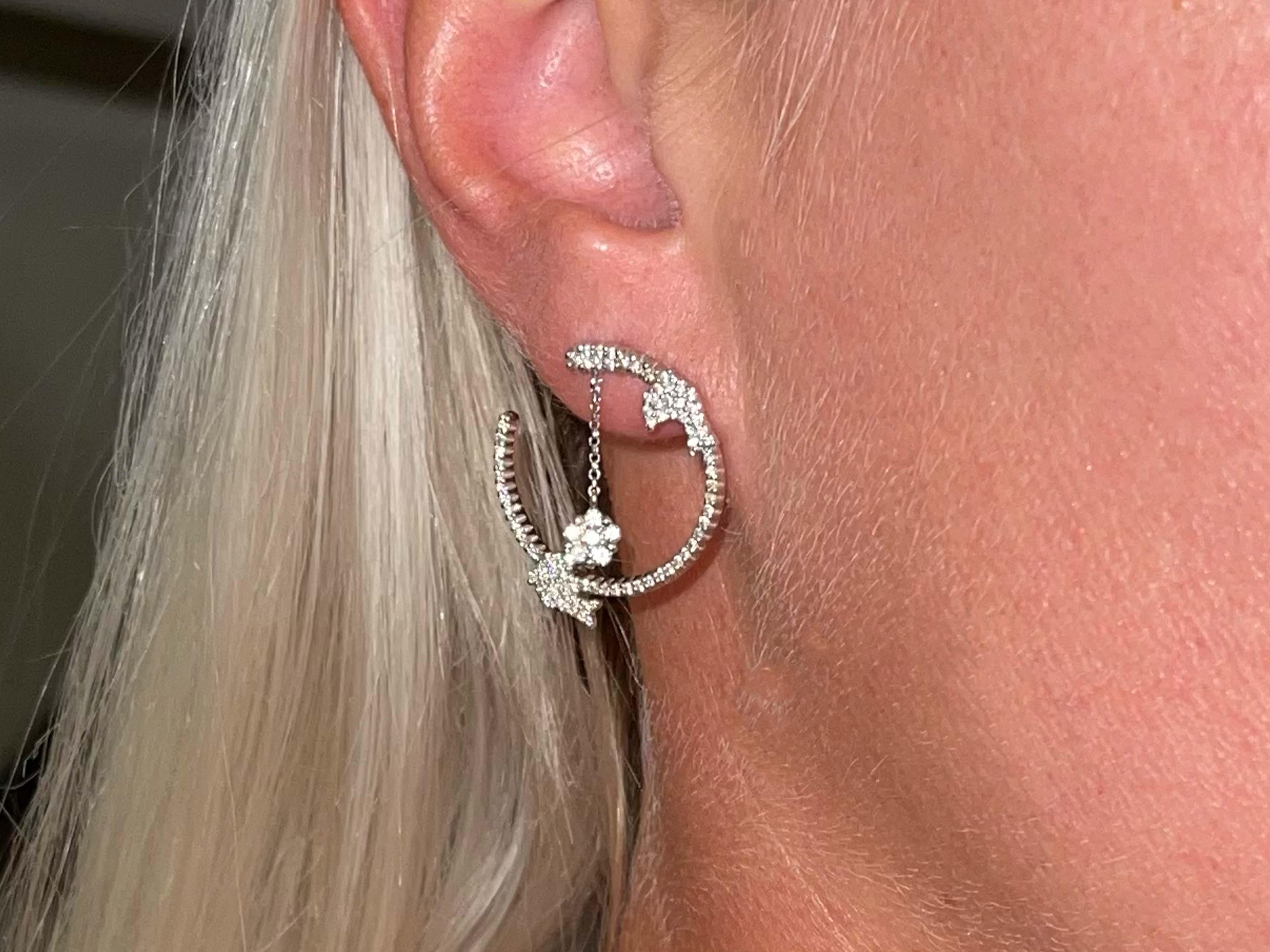 Crafted in 18K white gold, 86 round brilliant cut diamonds are set on each hoop creating a lifetime of timelessness. Two dolphins are perched on each hoop with a dangly flower in the middle giving the earring life and movement. The diamonds are G in