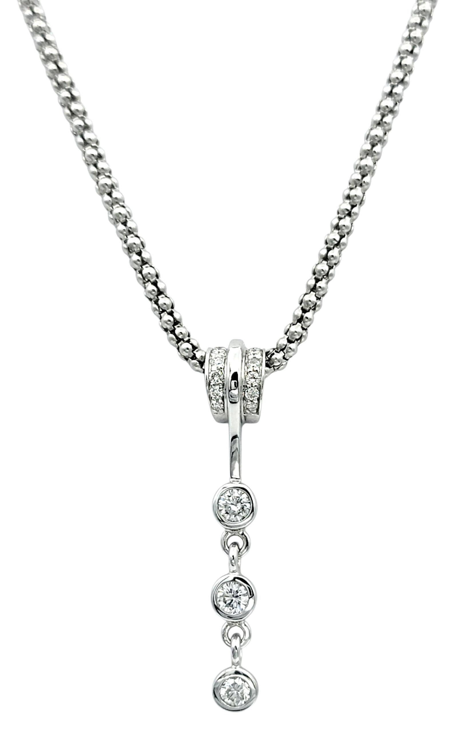 This elegant pendant necklace is crafted in 14 karat white gold and designed with timeless sophistication. The piece features a vertical drop of sparkling round brilliant cut diamonds, gracefully suspended from an 18-inch popcorn chain. Each diamond