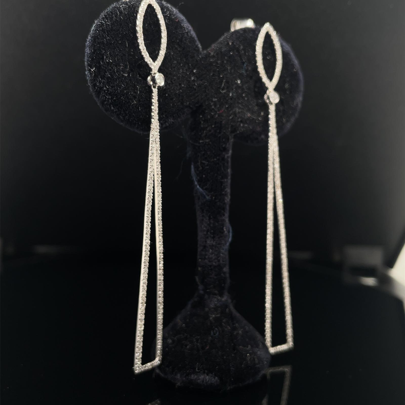 A pair of diamond drop earrings in 18 karat white gold.

Each elegant and contemporary earring comprises of a diamond set marquise outline atop a slim, elongated isosceles triangle. Set to the articulated join of each drop is a bezel set round