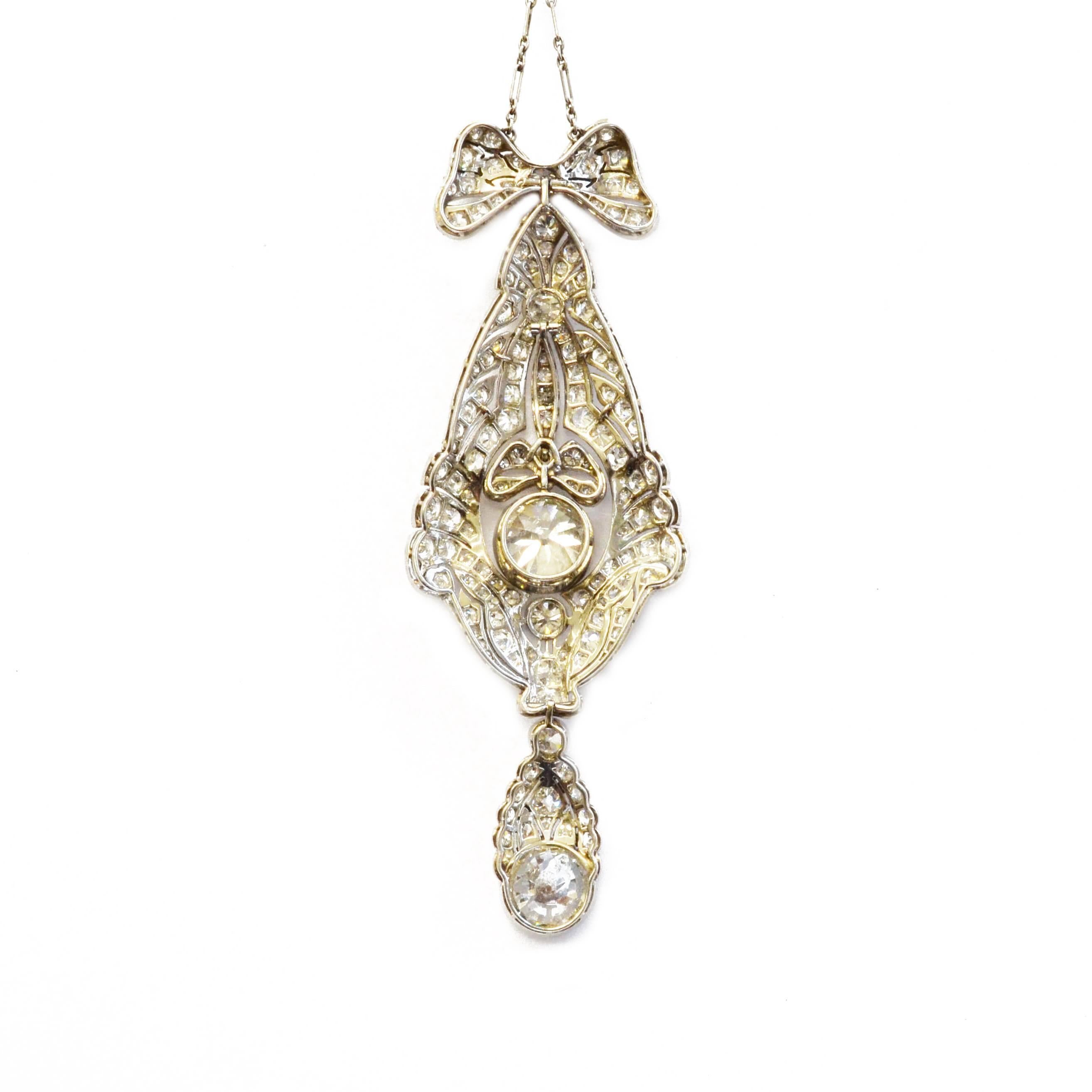 A Belle Epoque pendant of elongated design; pavé diamond set throughout. A bow suspends the decoratively pierced platinum drop which is fully articulated and centres on a substantial old cut diamond, and a further large old cut at the bottom.