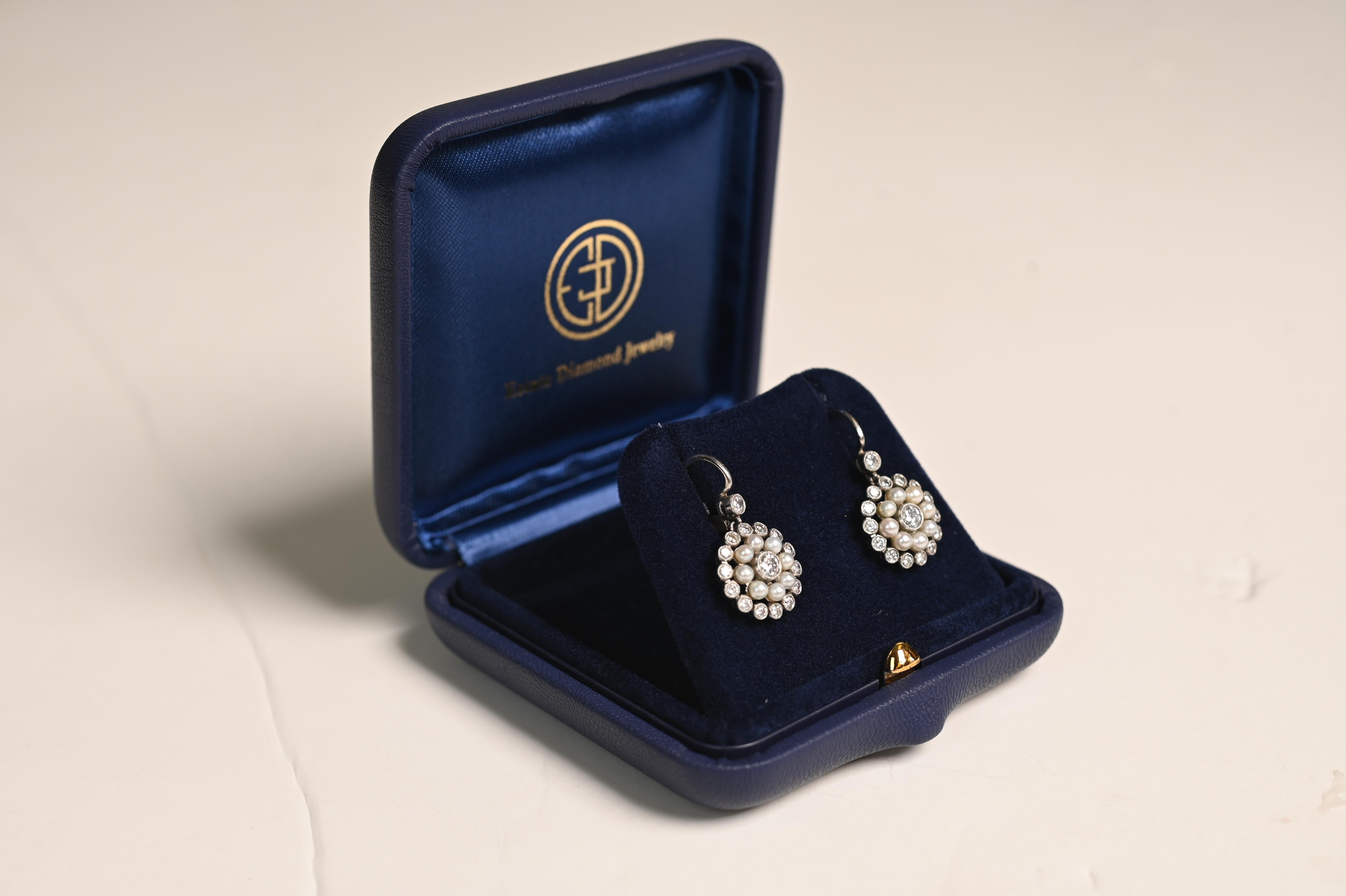 Questo squisito paio di orecchini in stile edoardiano mette in mostra l'eleganza senza tempo della lavorazione di perle e diamanti. Gli orecchini presentano un diamante centrale, del peso di circa 0,08 carati, circondato da una doppia aureola