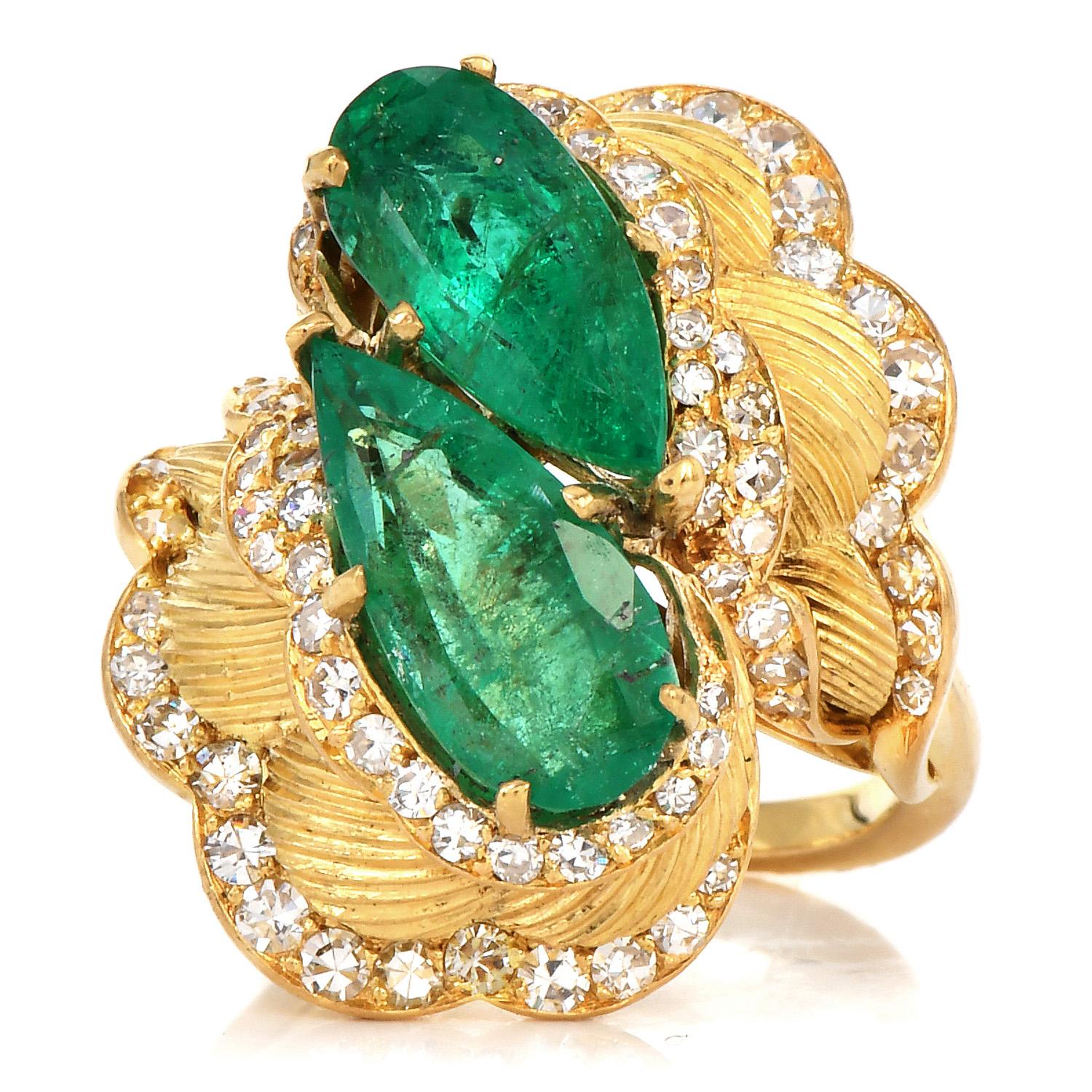 This vintage 1990s ring with a bypass style emeralds with diamonds is crafted in solid 18K Yellow Gold, with textured accents.

It weighs 11.8 grams and incorporates a scalloped vertical texture with diamond-accented borders.

The vivid green center