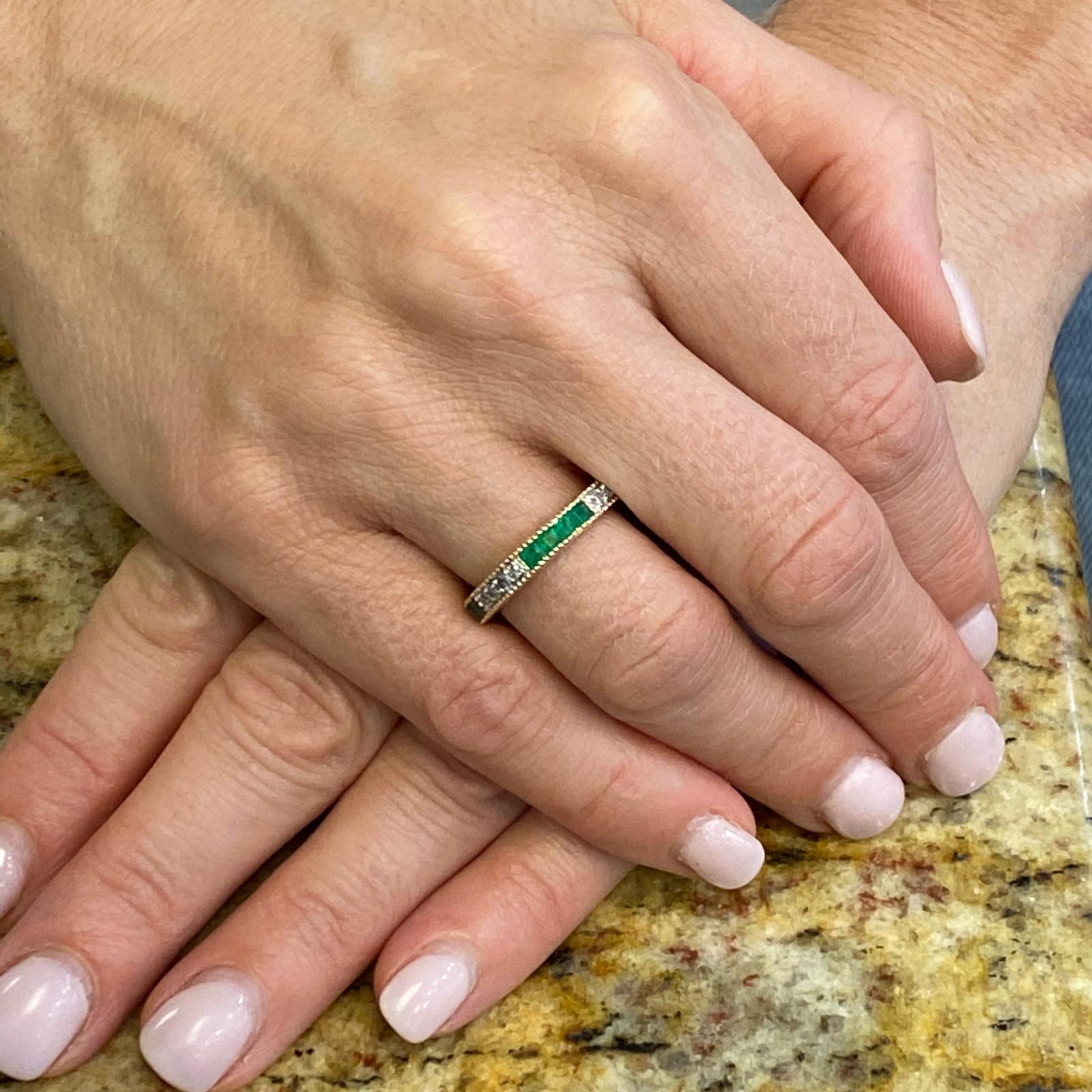 Diamond and emerald eternity band ring fashioned in 14 karat yellow gold. The band features 7 round brilliant cut diamonds weighing .21 carat total weight and 8 square cut natural emeralds weighing .64 carat total weight. The diamonds are graded G-H