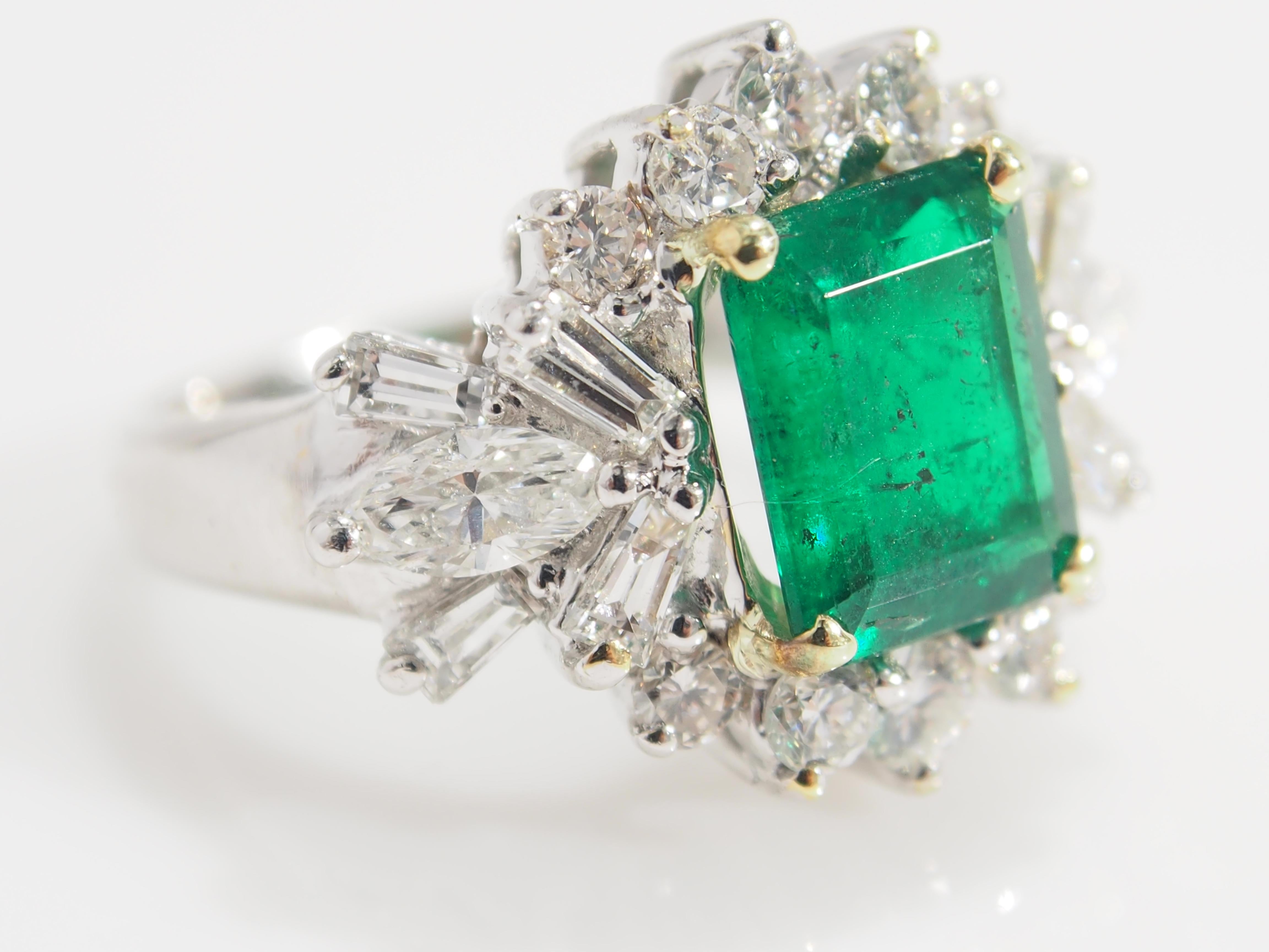 This is an alluring 18K White Gold Diamond and Emerald Ring which measures 3/4 inch in length and 1/2 inch in width. A lustrous Diamond Cluster designed with (2) Marquise Diamonds, (8) Baguettes and (10) Round Brilliant Cut Diamonds for an