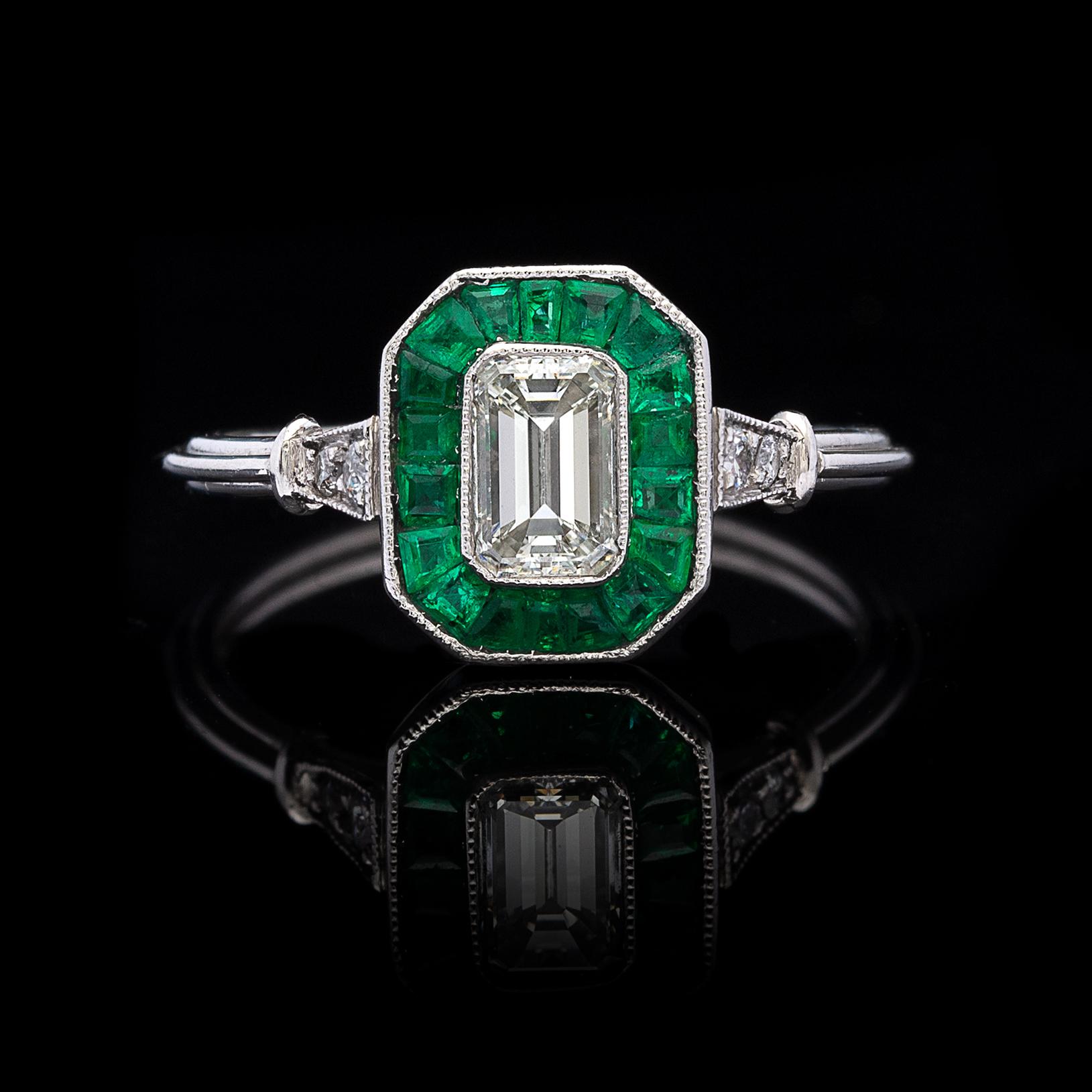 Hark back to an era of fine design with this lovely Art Deco inspired 18k white gold ring! It centers a bezel-set emerald-cut diamond, weighing an estimated 0.50 carat, G/VS, set within a frame of calibre-cut emeralds, and then highlighted with 4